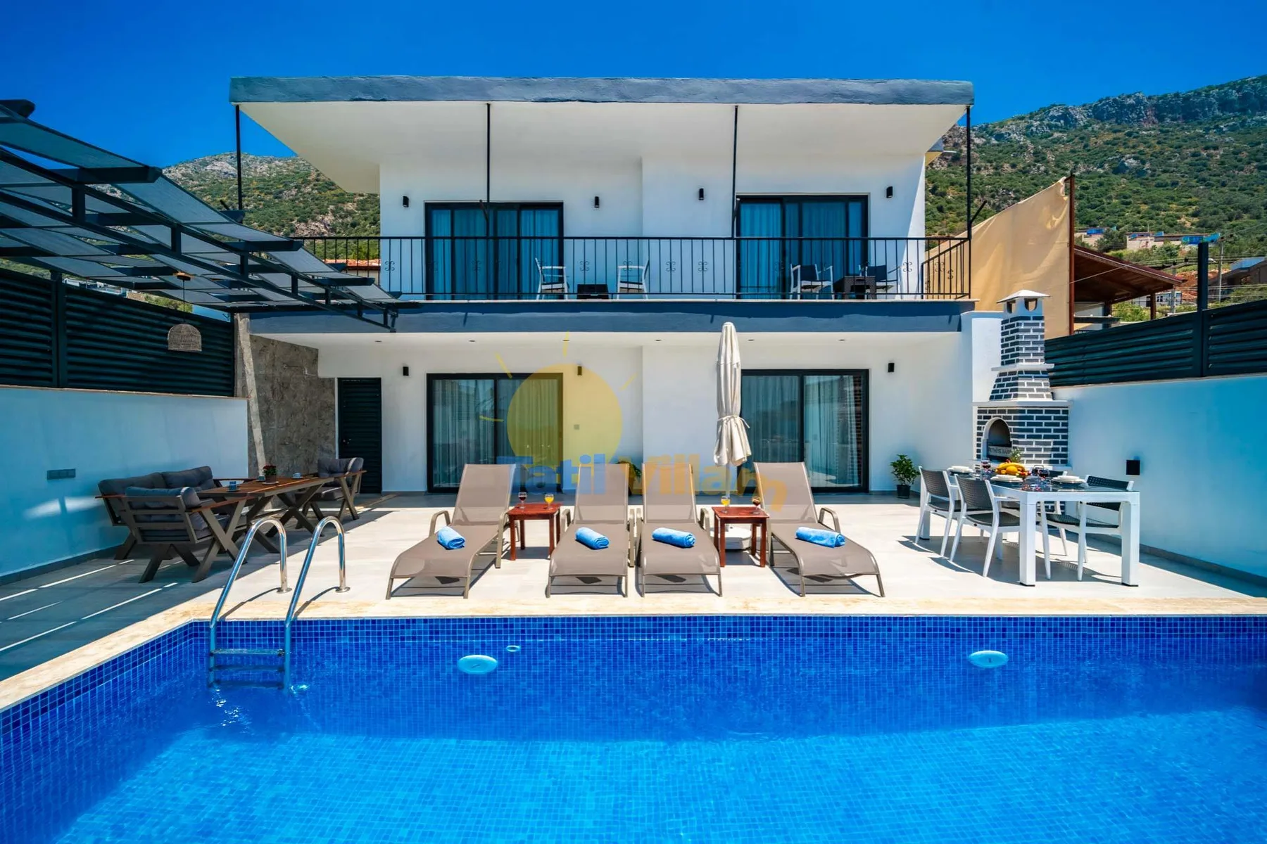 A modern two-story house overlooks a swimming pool, with loungers on the patio.