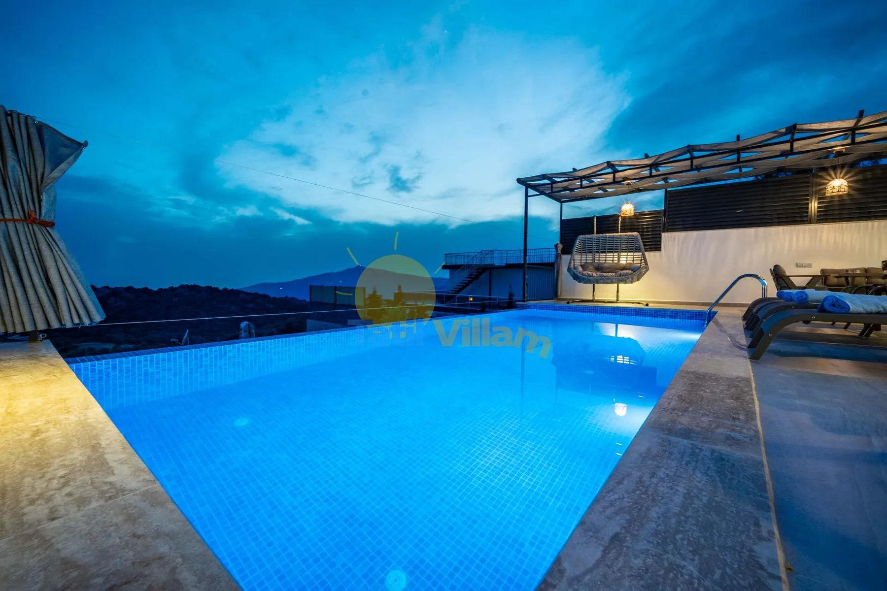 An outdoor swimming pool glows blue beneath a cloudy evening sky.