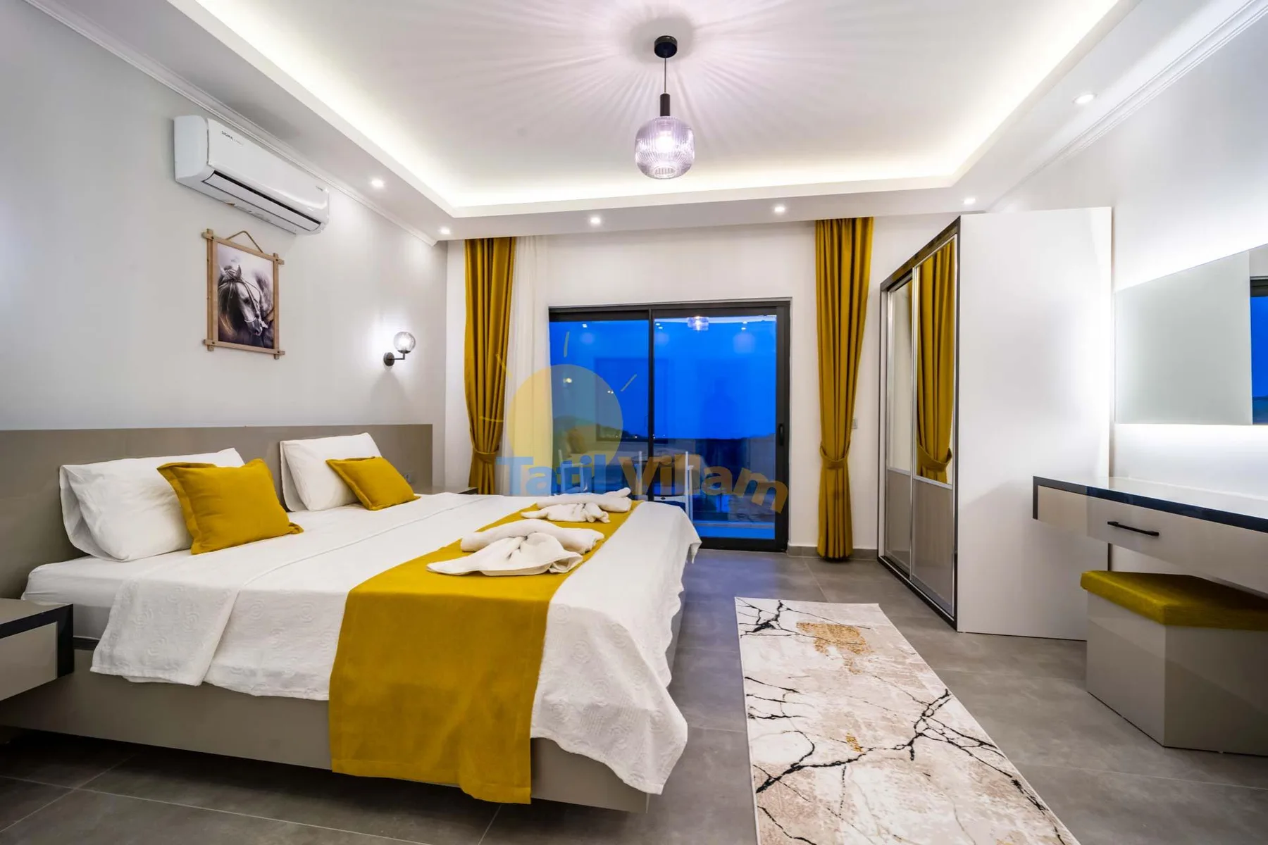 A bedroom with white bedding, yellow accents, and a glass door opening onto a balcony.