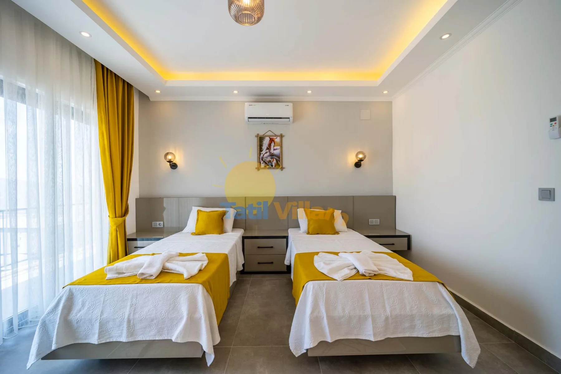 A bedroom with two single beds, yellow bedding, and a window with sheer curtains.