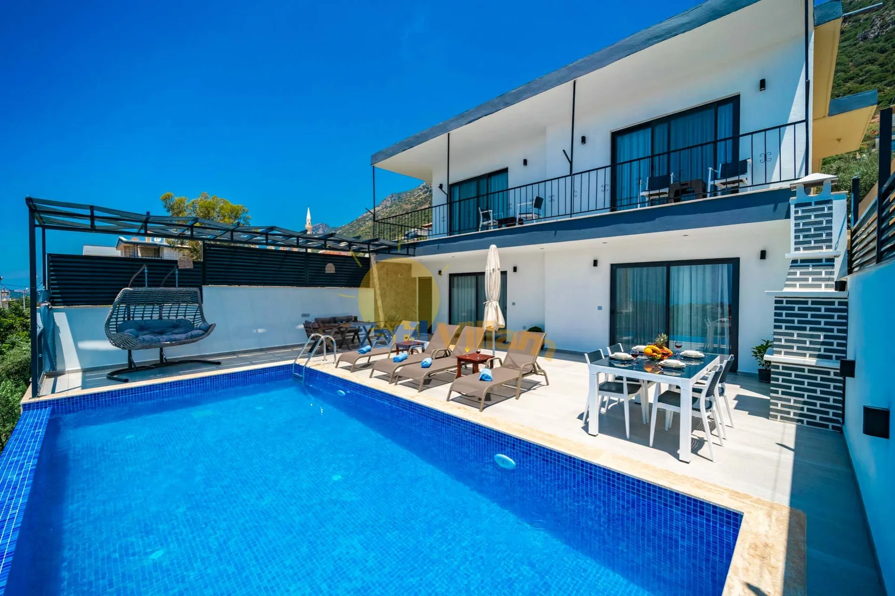 A modern house overlooks a swimming pool and patio seating.