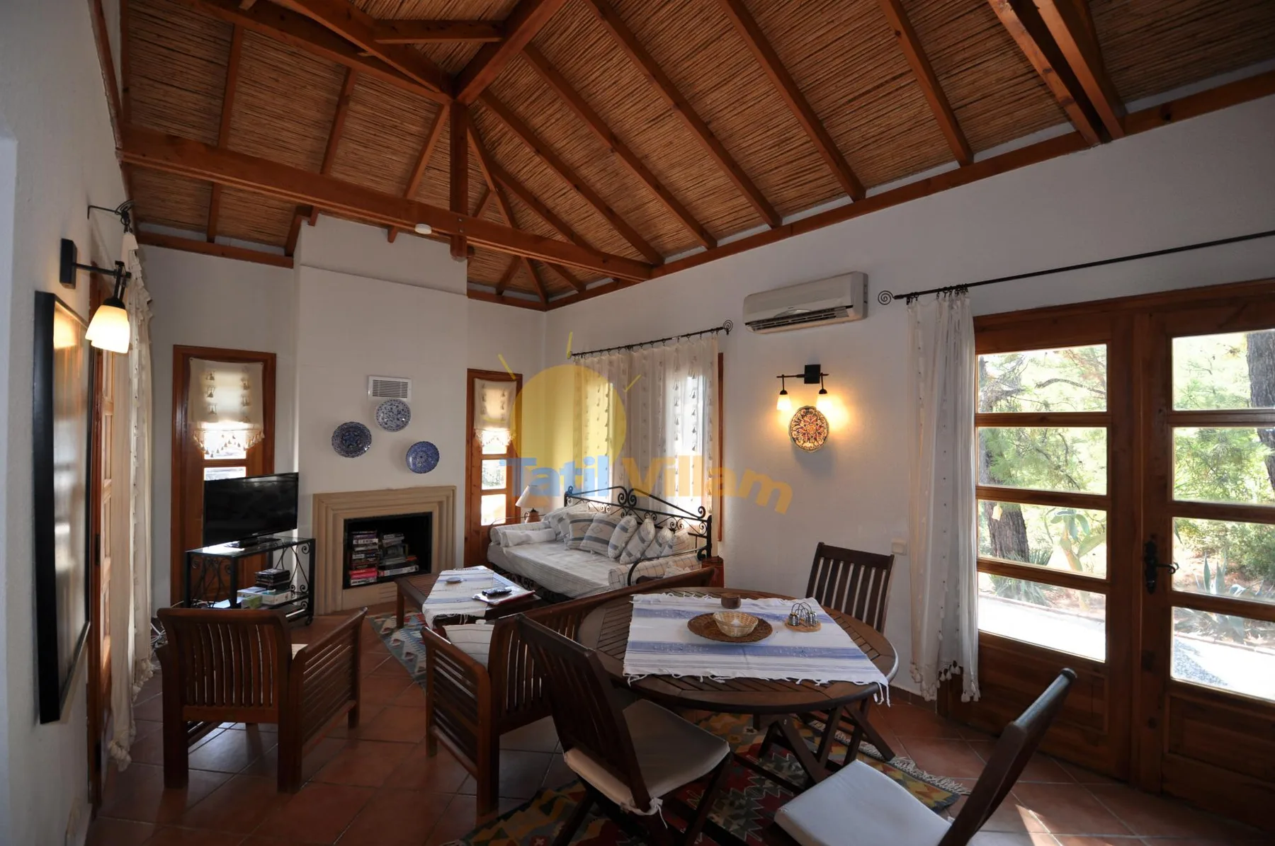 A dining and living area with a wooden table, seating, and a high timber ceiling.