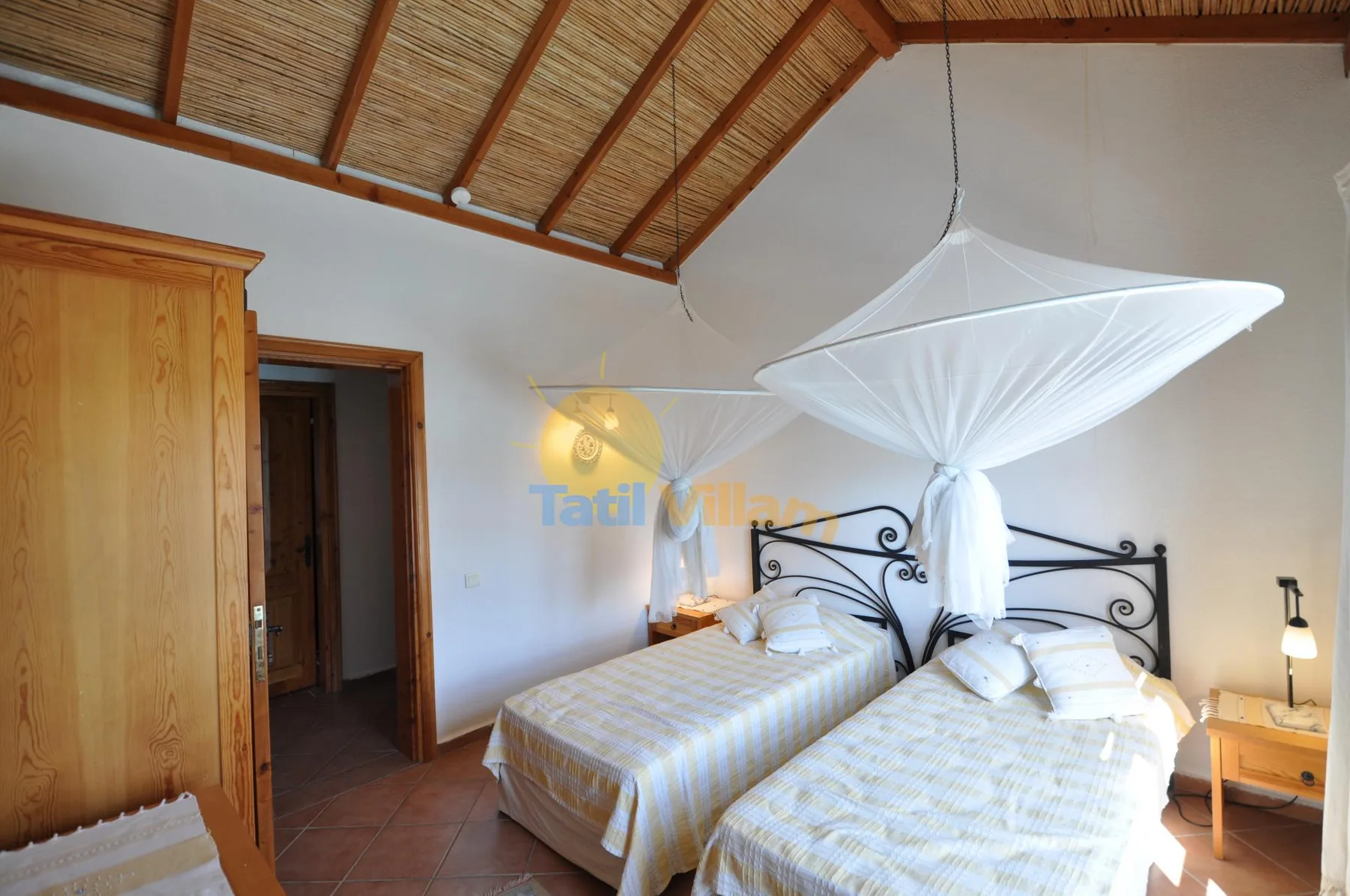 A bedroom with two beds, a wooden wardrobe, and a draped canopy.