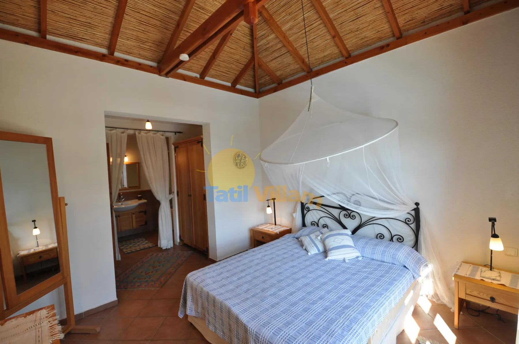 A bedroom with a large bed beneath a peaked wood-beam ceiling.