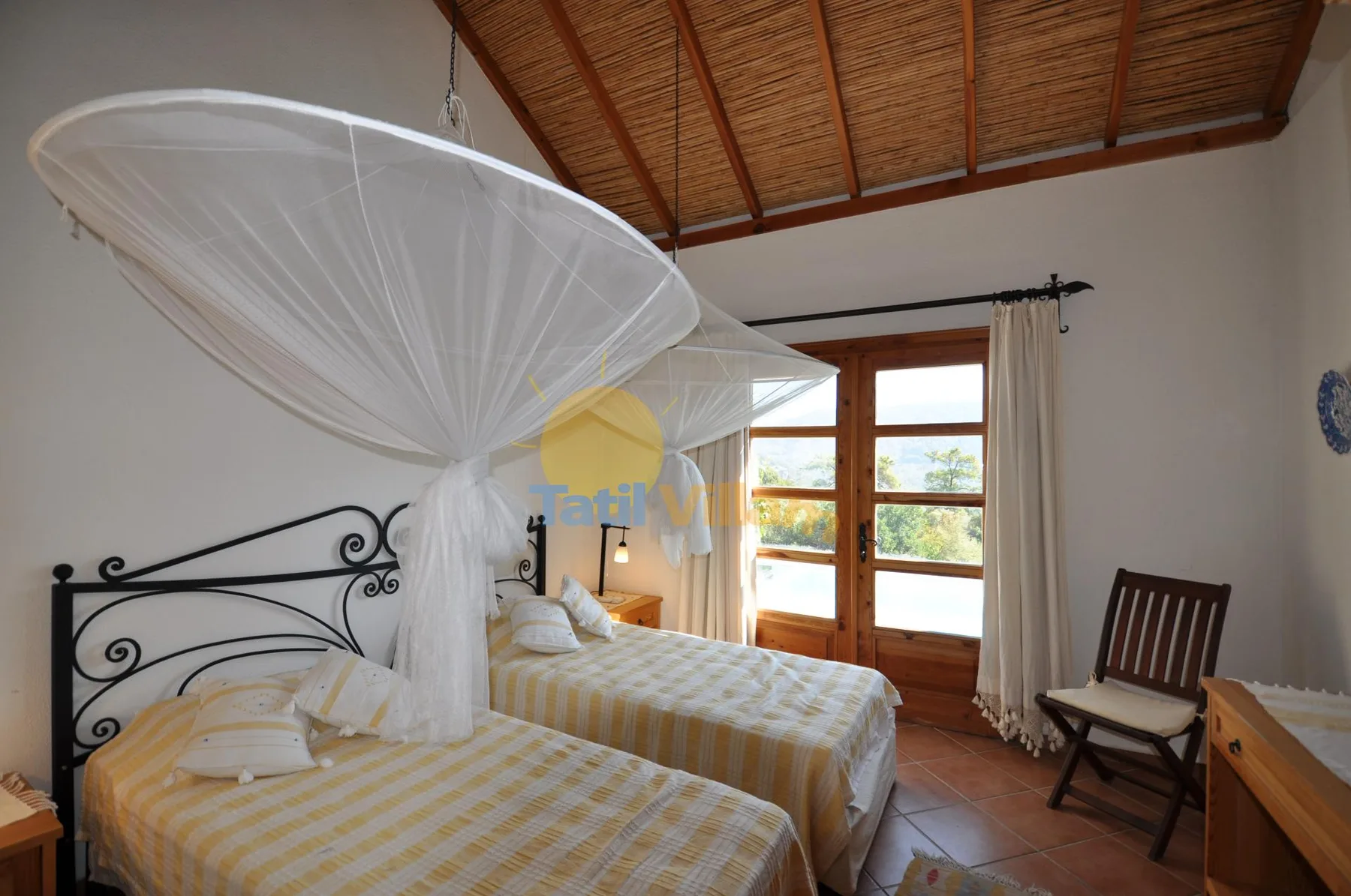 A bedroom with two beds beneath a draped canopy and wooden ceiling.