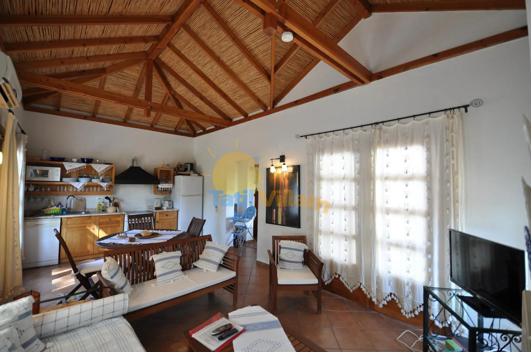 A bright open-plan living room and kitchen with seating beneath a timber ceiling.