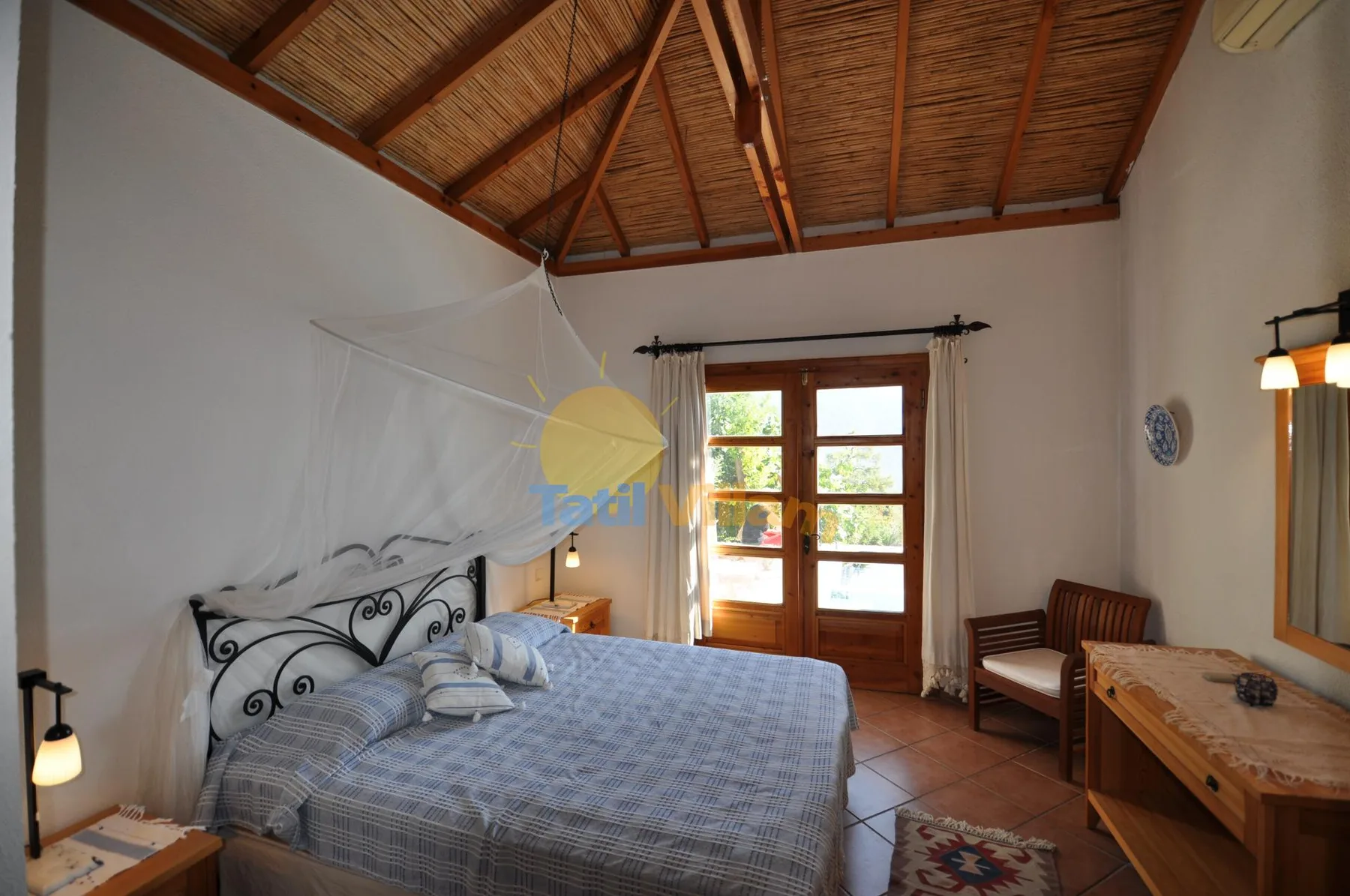 A bedroom with a bed, wooden ceiling, and glass doors opening to a balcony.