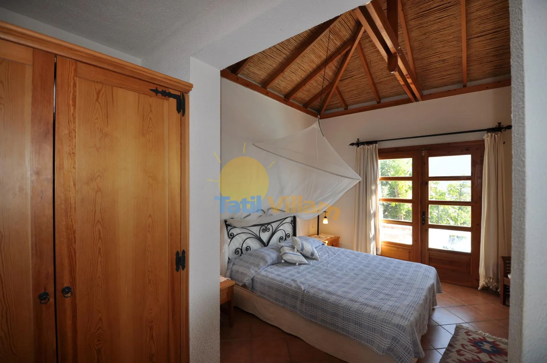 A bedroom with a bed beneath a sloped wooden ceiling and a bright window.