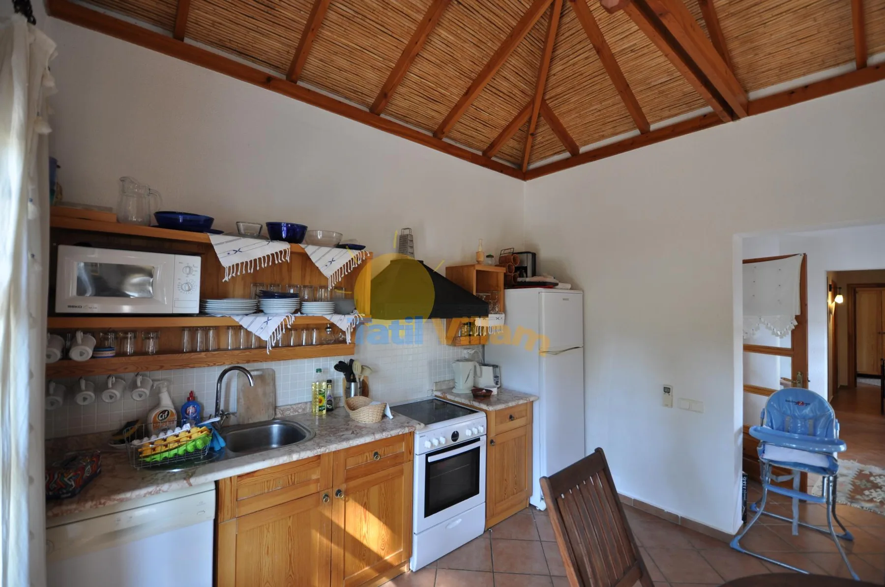 A kitchen with wooden cabinets and a high, exposed-beam ceiling.