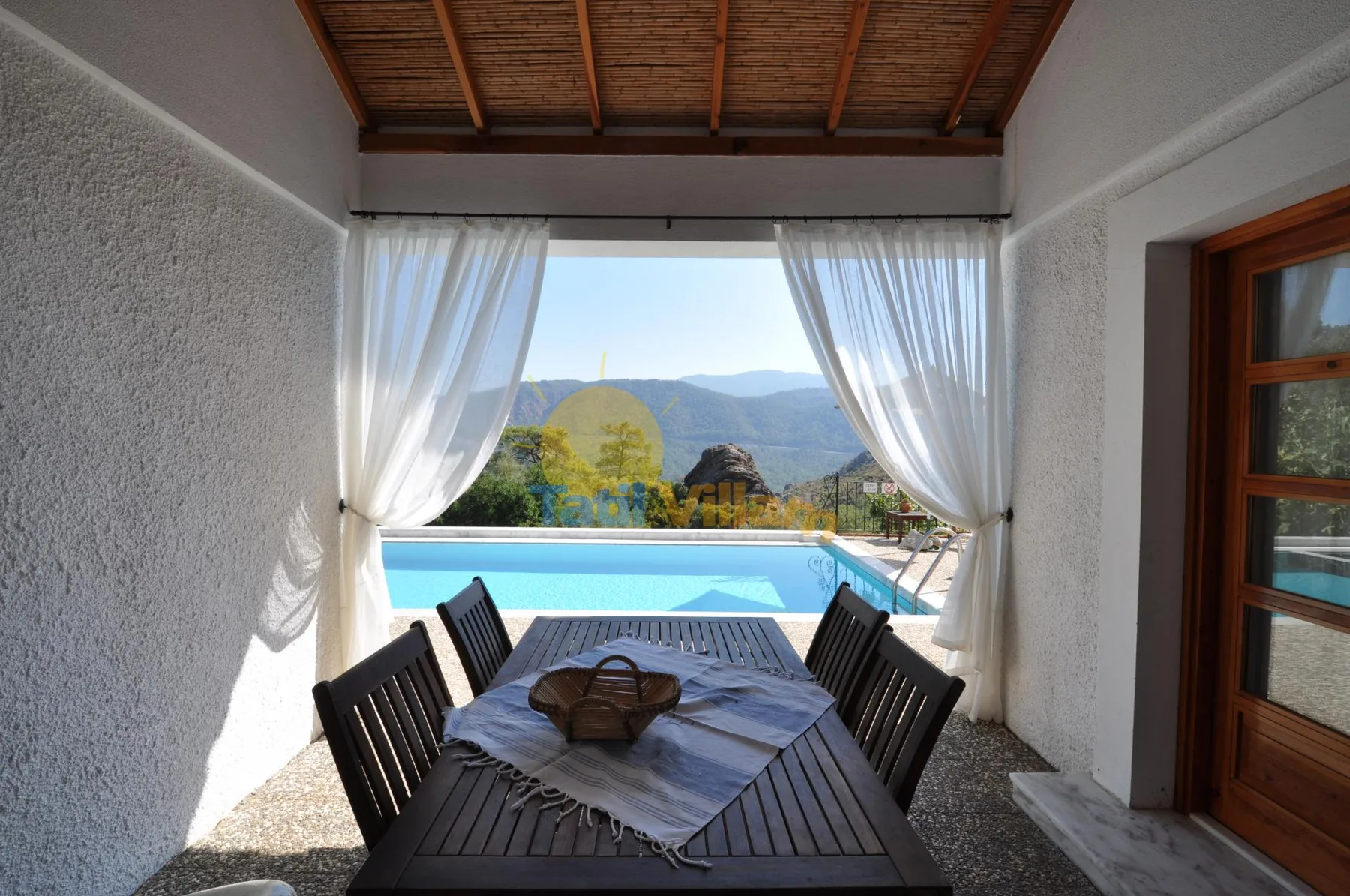 A dining area opens onto a pool and mountain view through sheer curtains.