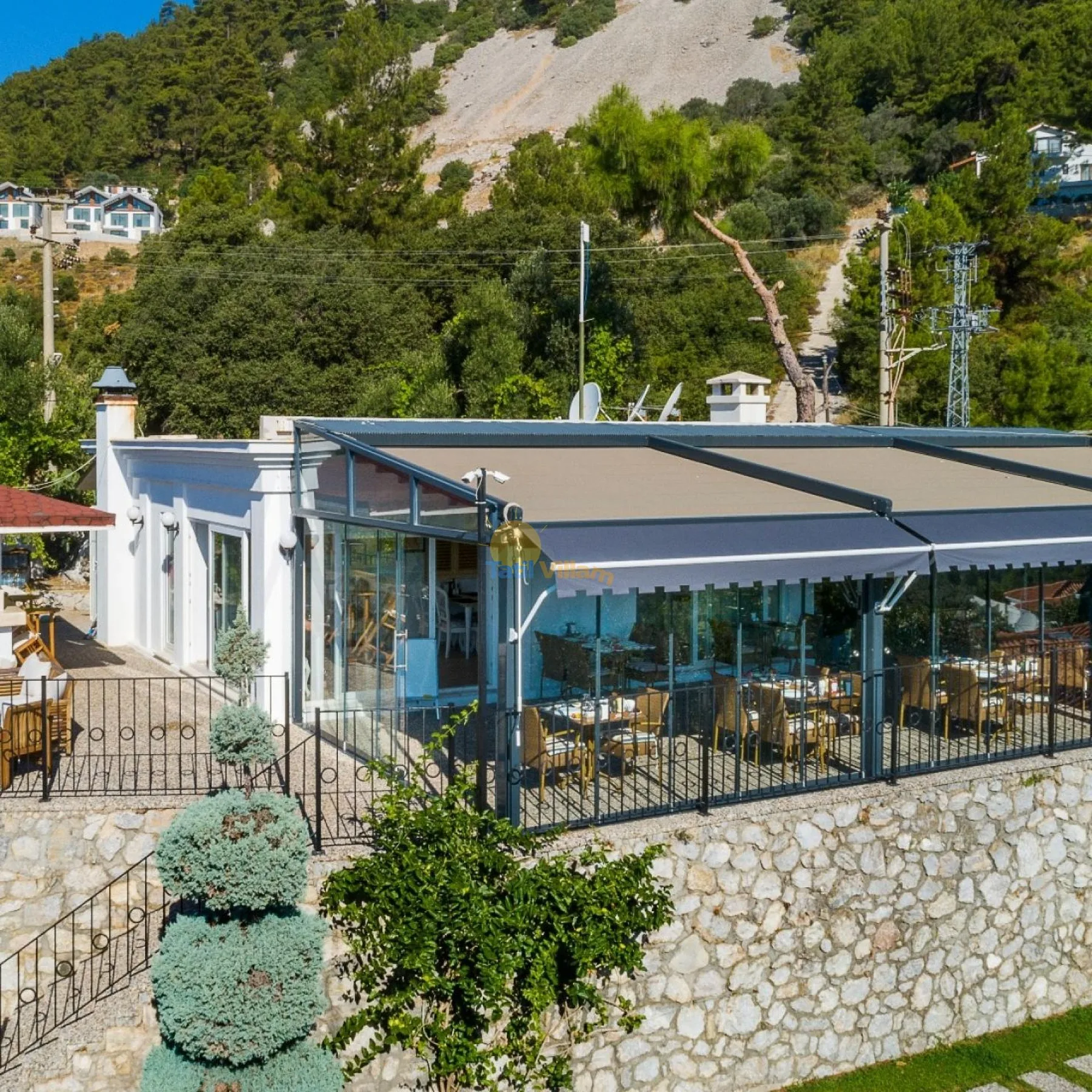 Zona común: Una zona de comedor acristalada está bajo un amplio toldo junto a un muro de piedra.