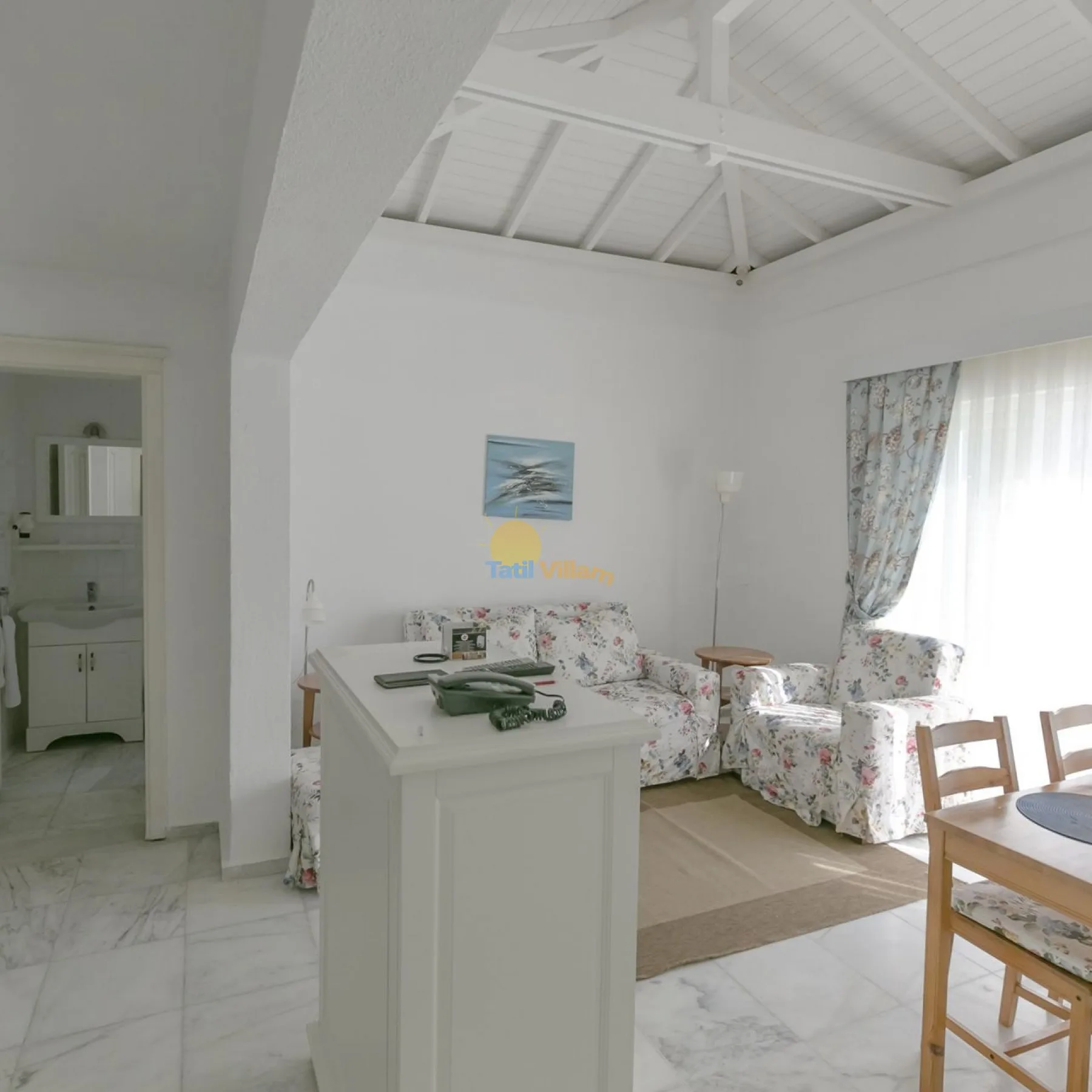 Una luminosa sala de estar y comedor con asientos florales, una mesa y un alto techo blanco.