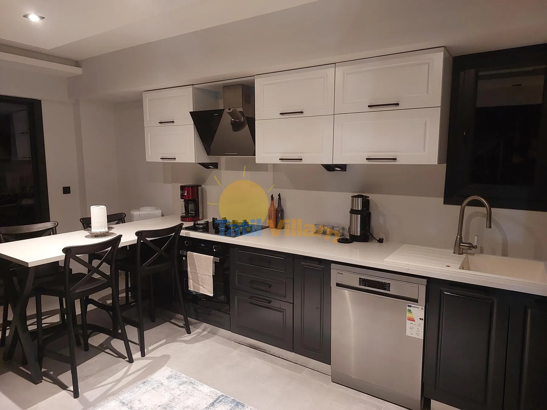 Una cocina moderna con gabinetes blancos, armarios oscuros y una barra con asientos.