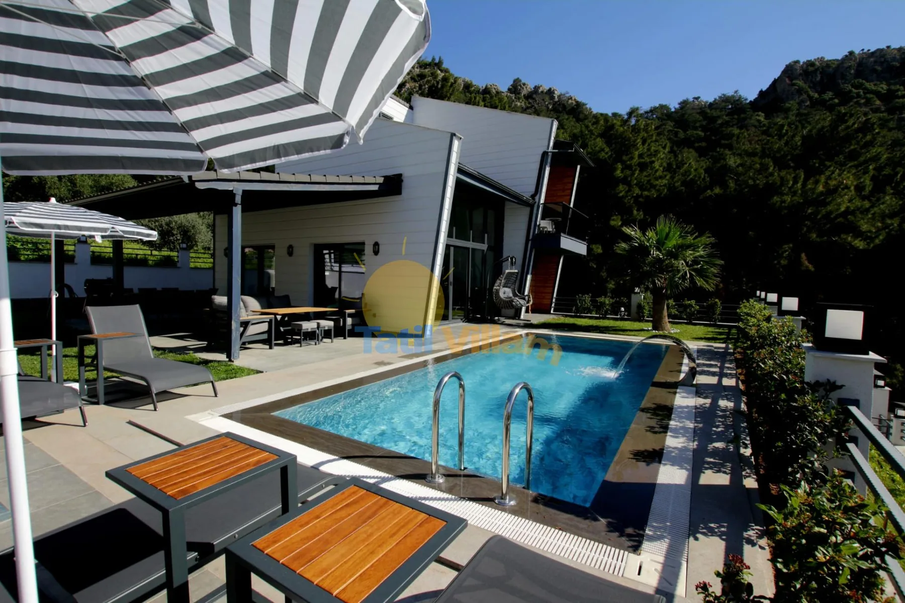 Una piscina al aire libre está junto a un edificio moderno y una zona de estar con sombra.