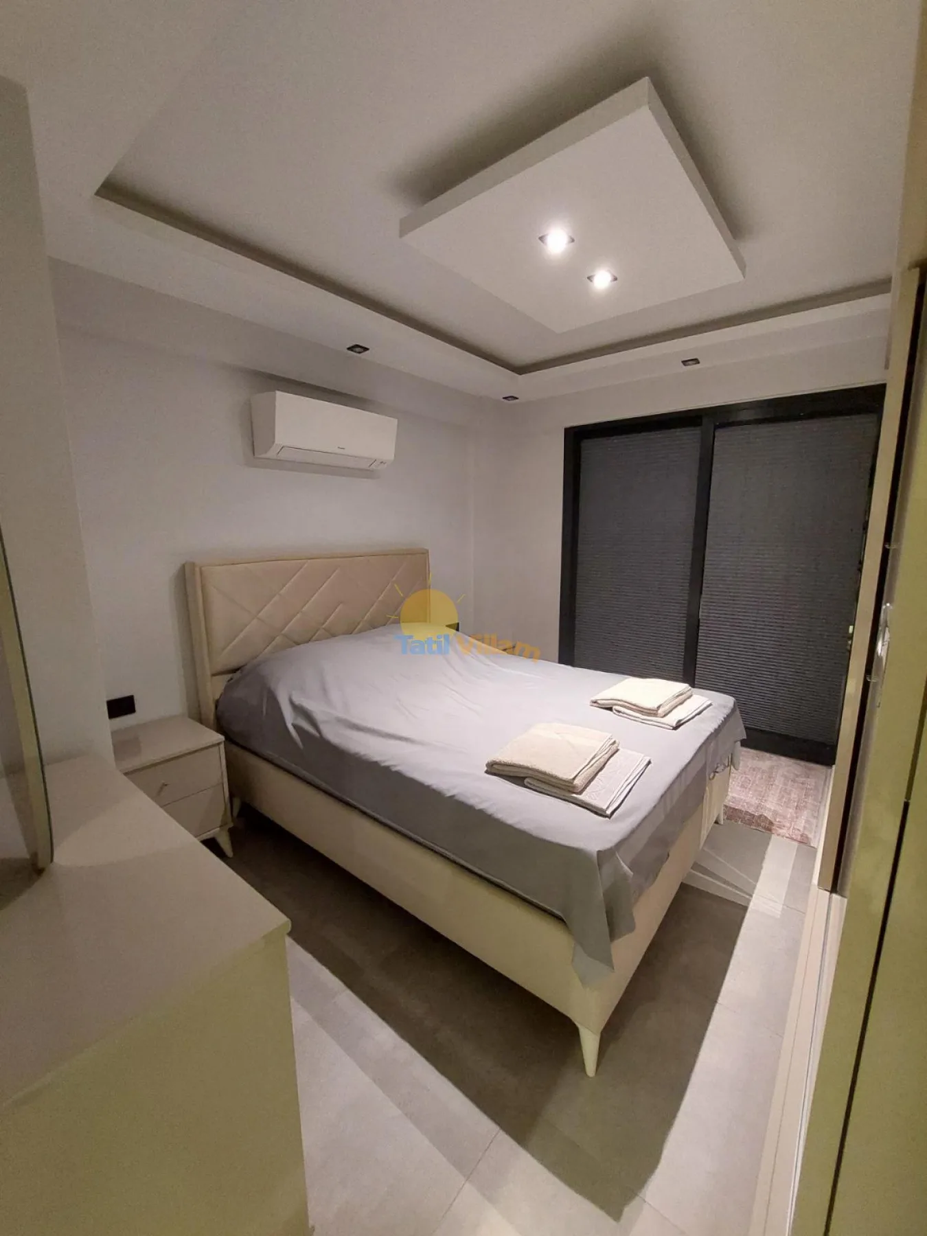 Un dormitorio con una cama ordenada y cortinas oscuras en la ventana.