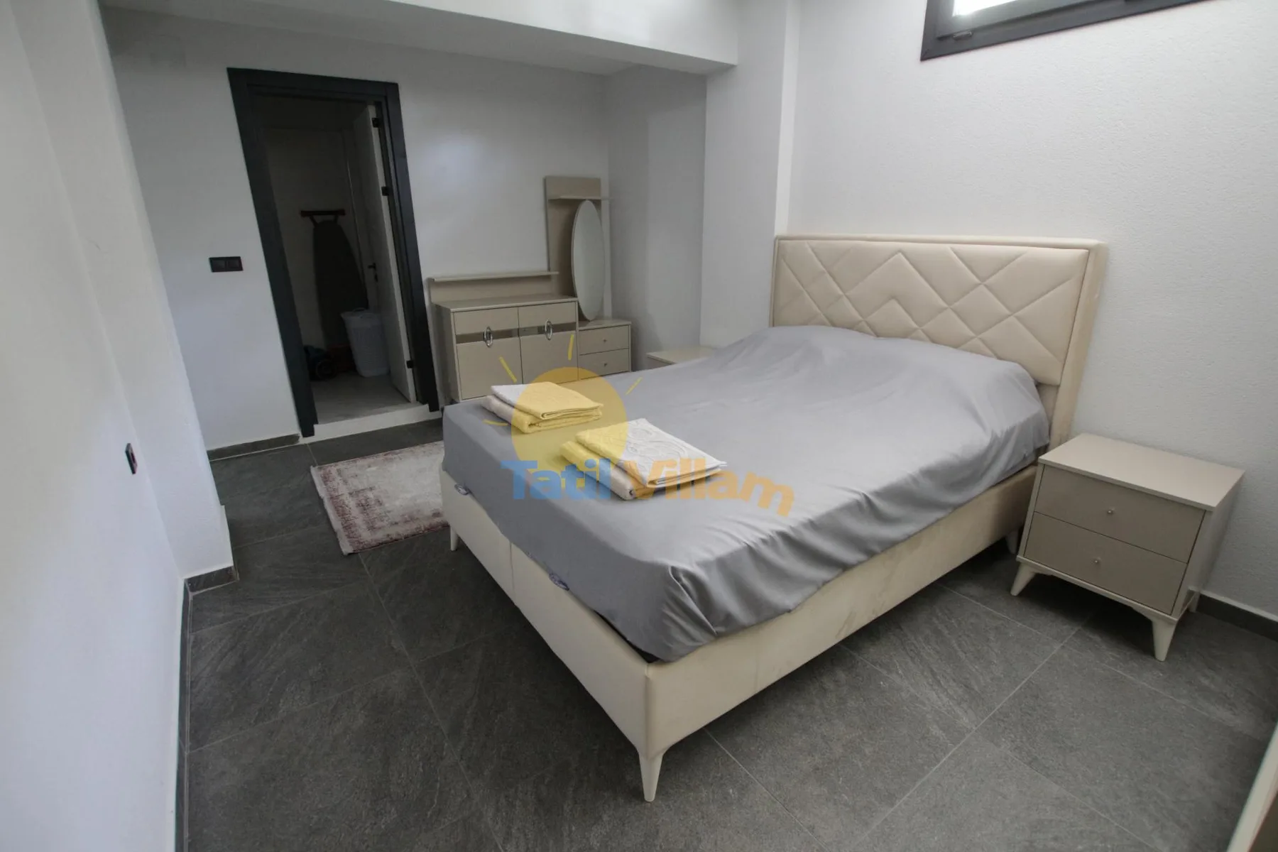 Un dormitorio con una cama, una mesita de noche y suelo de baldosas oscuras.