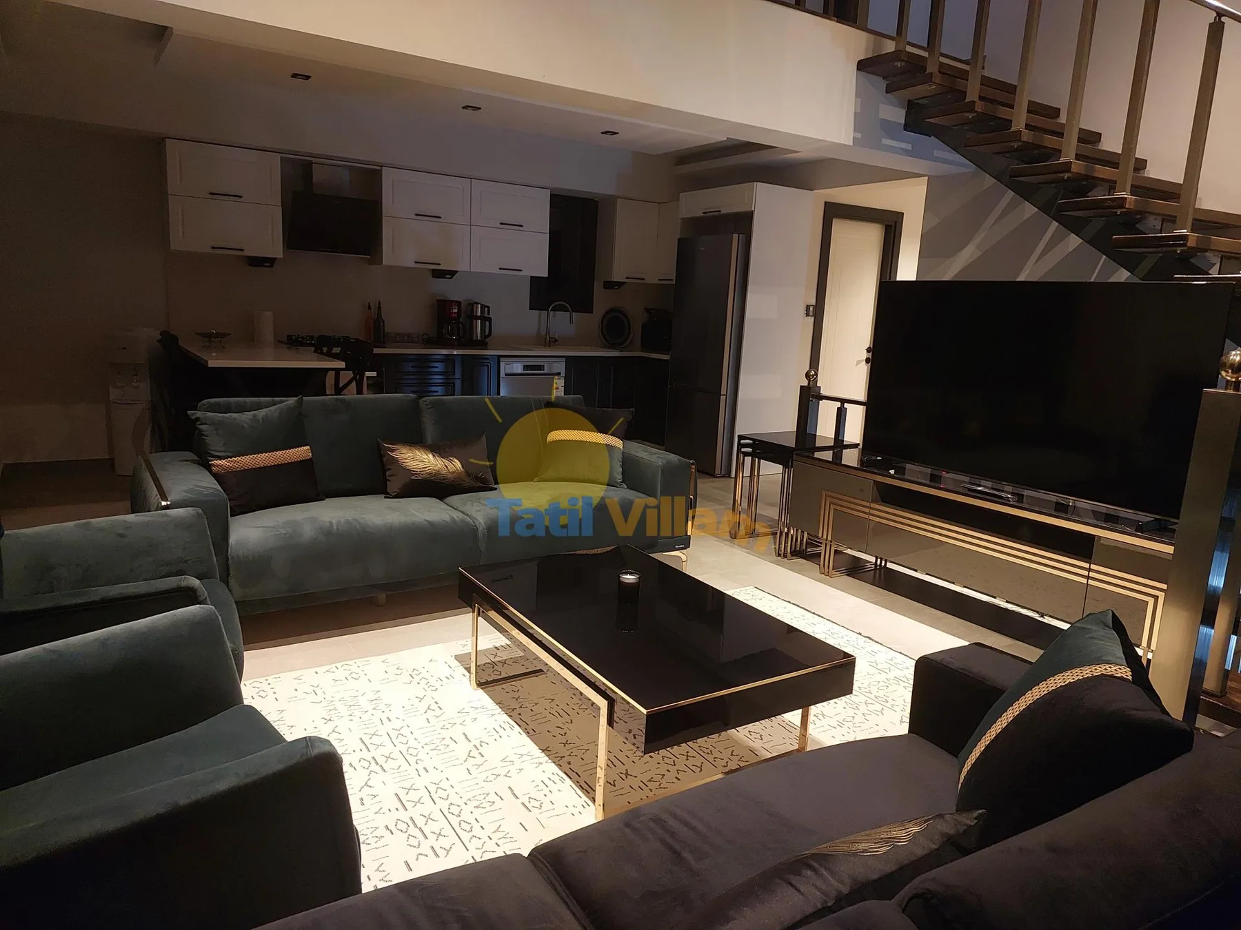 Una sala de estar con asientos, una mesa de centro y un televisor junto a una cocina abierta.