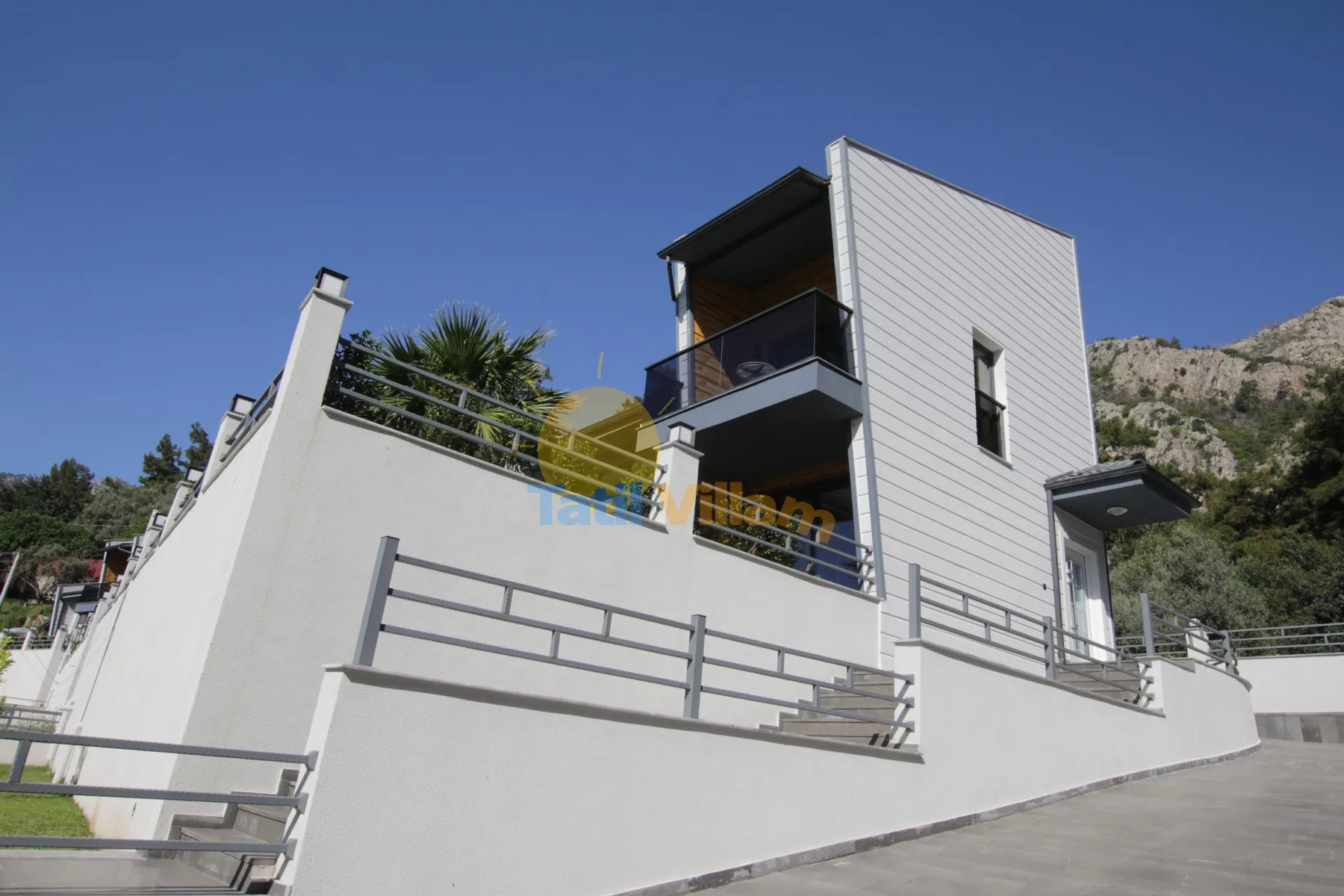 Un edificio blanco moderno con balcones se alza bajo un cielo azul despejado.
