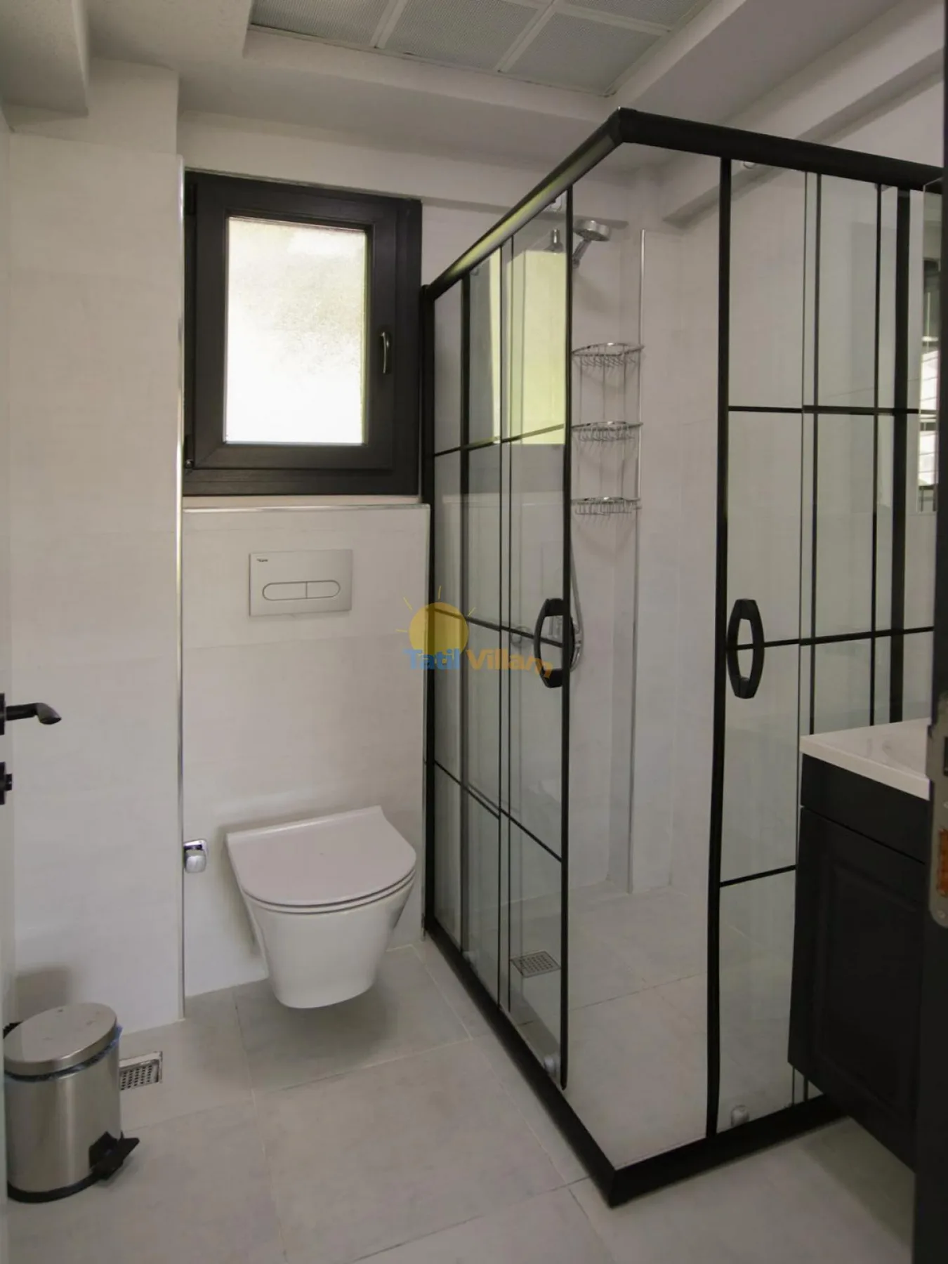 Un baño con inodoro, ducha de vidrio y un mueble oscuro.