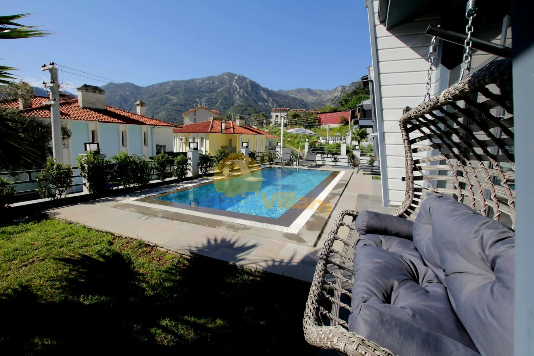 Una piscina al aire libre junto a un asiento colgante acolchado, con montañas al fondo.