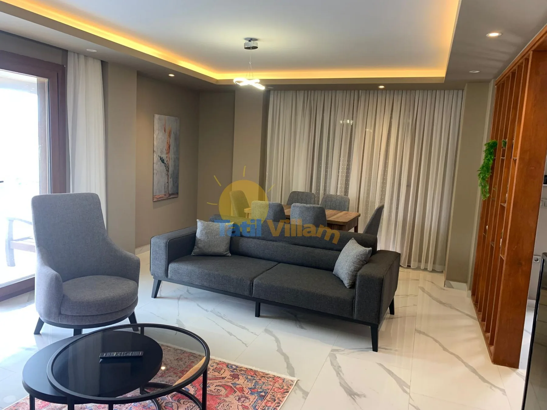 A living room with gray seating, a round coffee table, and floor-length curtains.