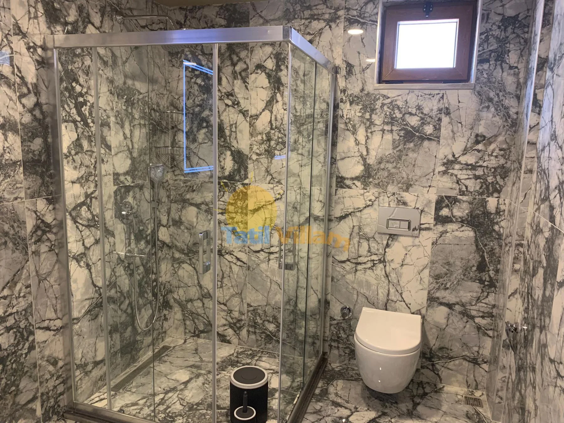 A bathroom with a glass shower and a wall-mounted toilet.
