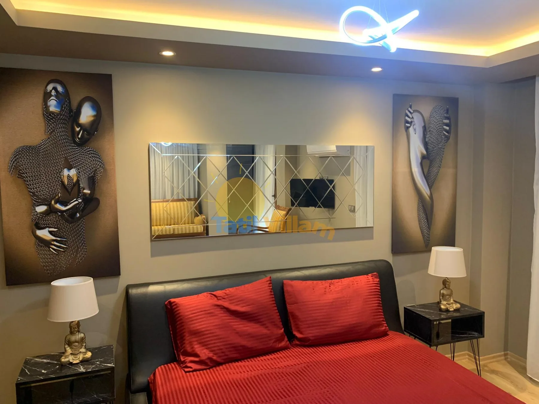 A bedroom with a bed, red bedding, wall art, and bedside tables.