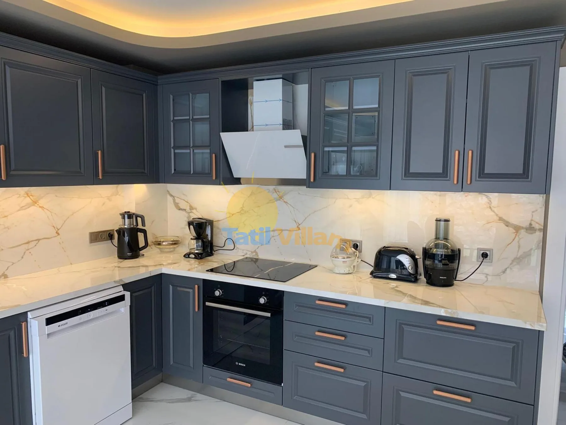A modern kitchen with dark cabinets, a cooktop, and countertop appliances.