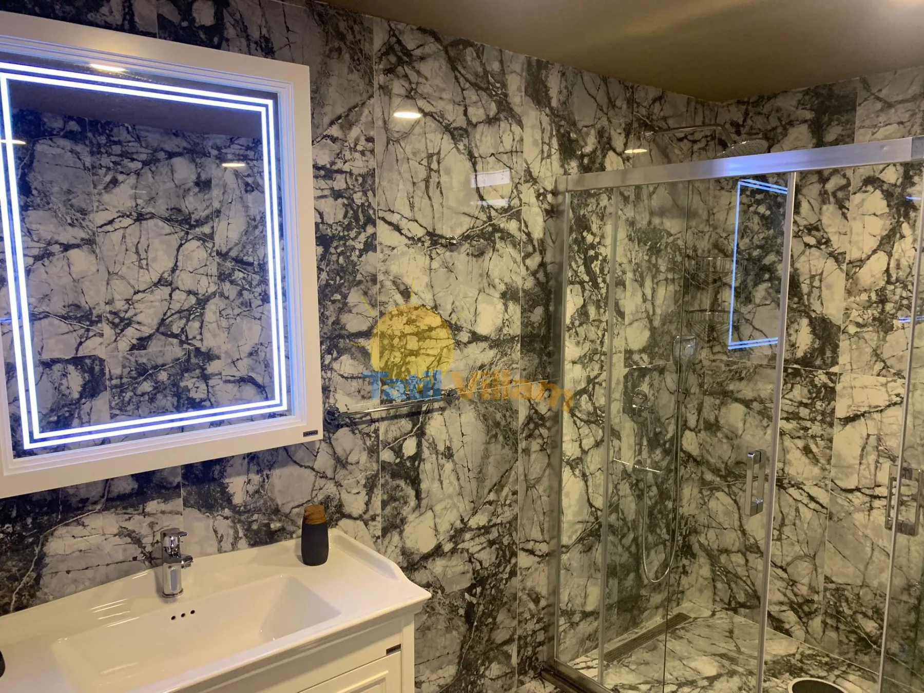 A bathroom with a sink, illuminated mirror, and glass shower.