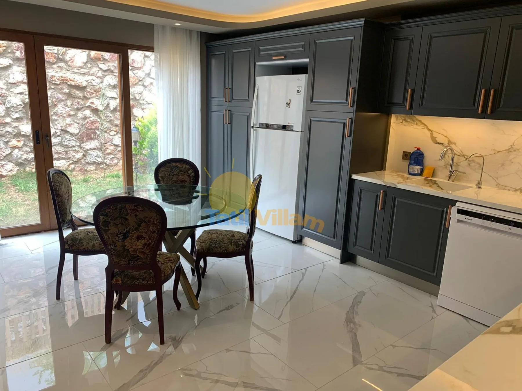 A kitchen dining area with dark cabinetry, a refrigerator, and a glass table.