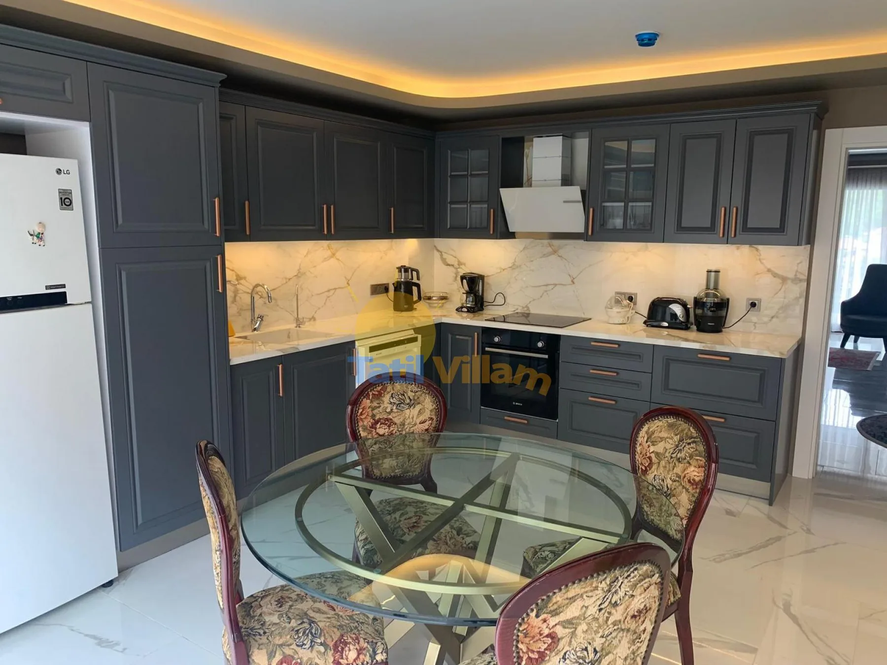 A modern kitchen with dark cabinetry, marble-patterned counters, and a glass dining table.