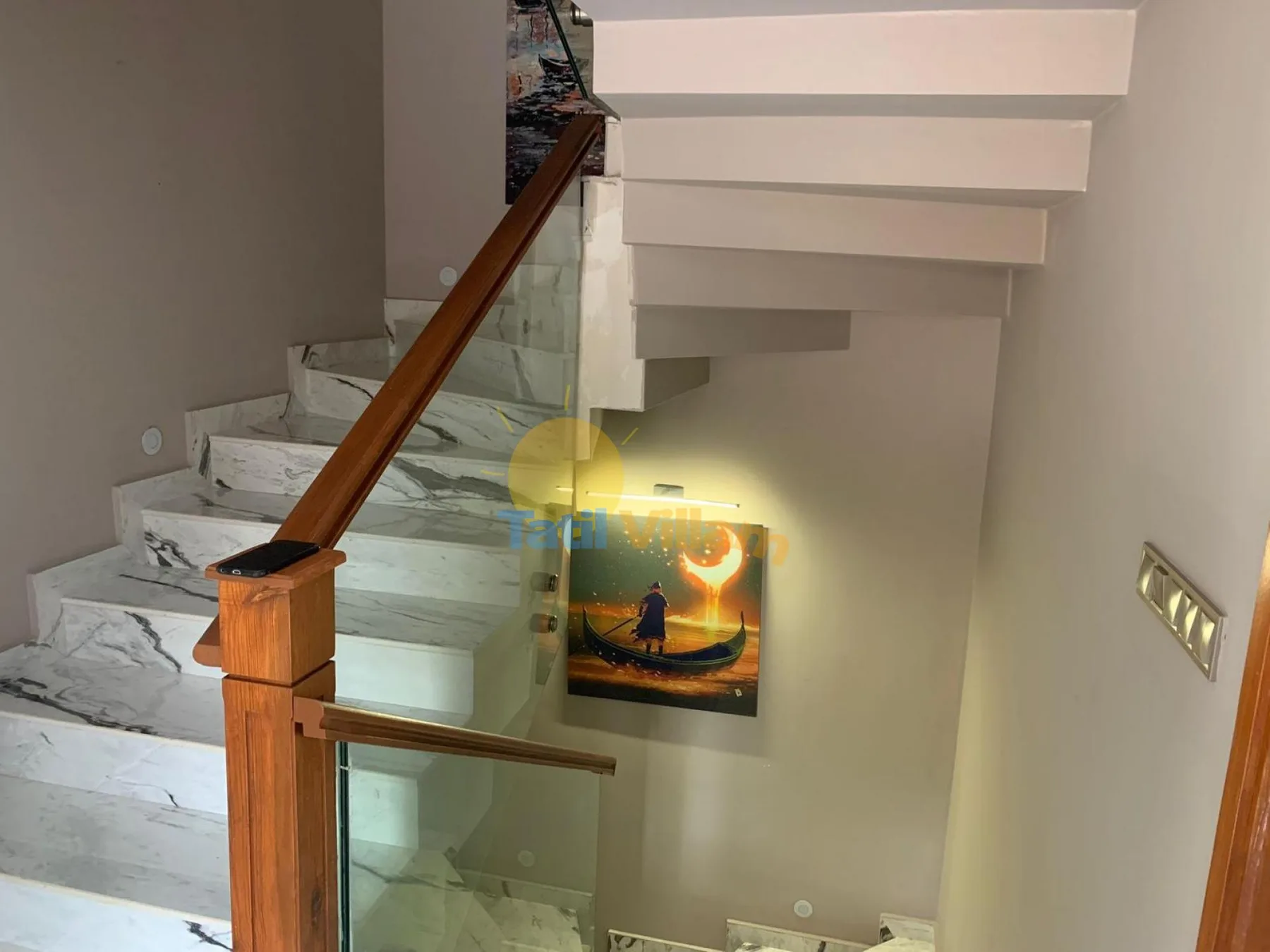 An indoor staircase with marble-patterned steps, a glass railing, and a wooden handrail.