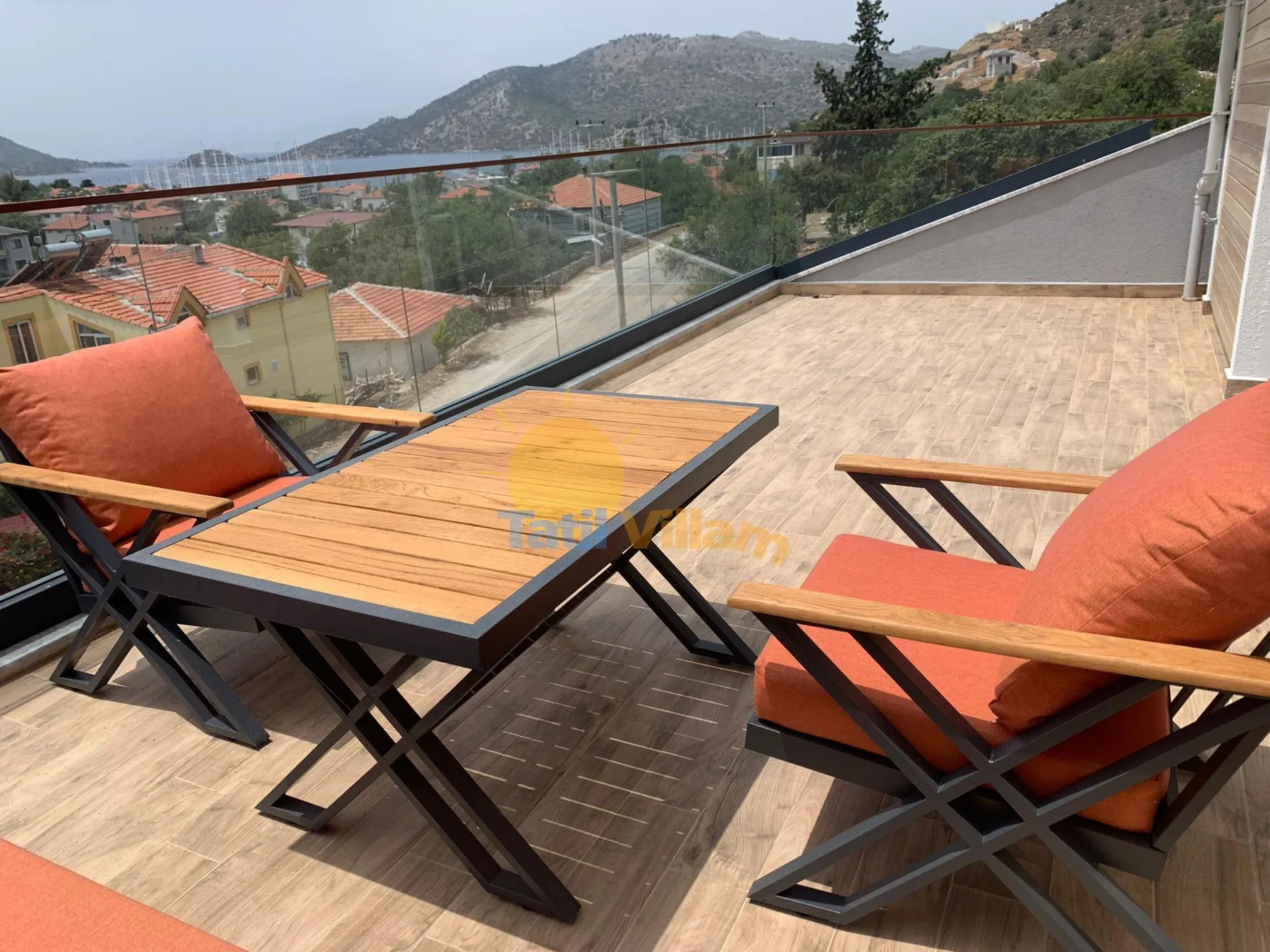 A terrace with a wooden table and orange cushioned seating overlooks the surrounding hills.