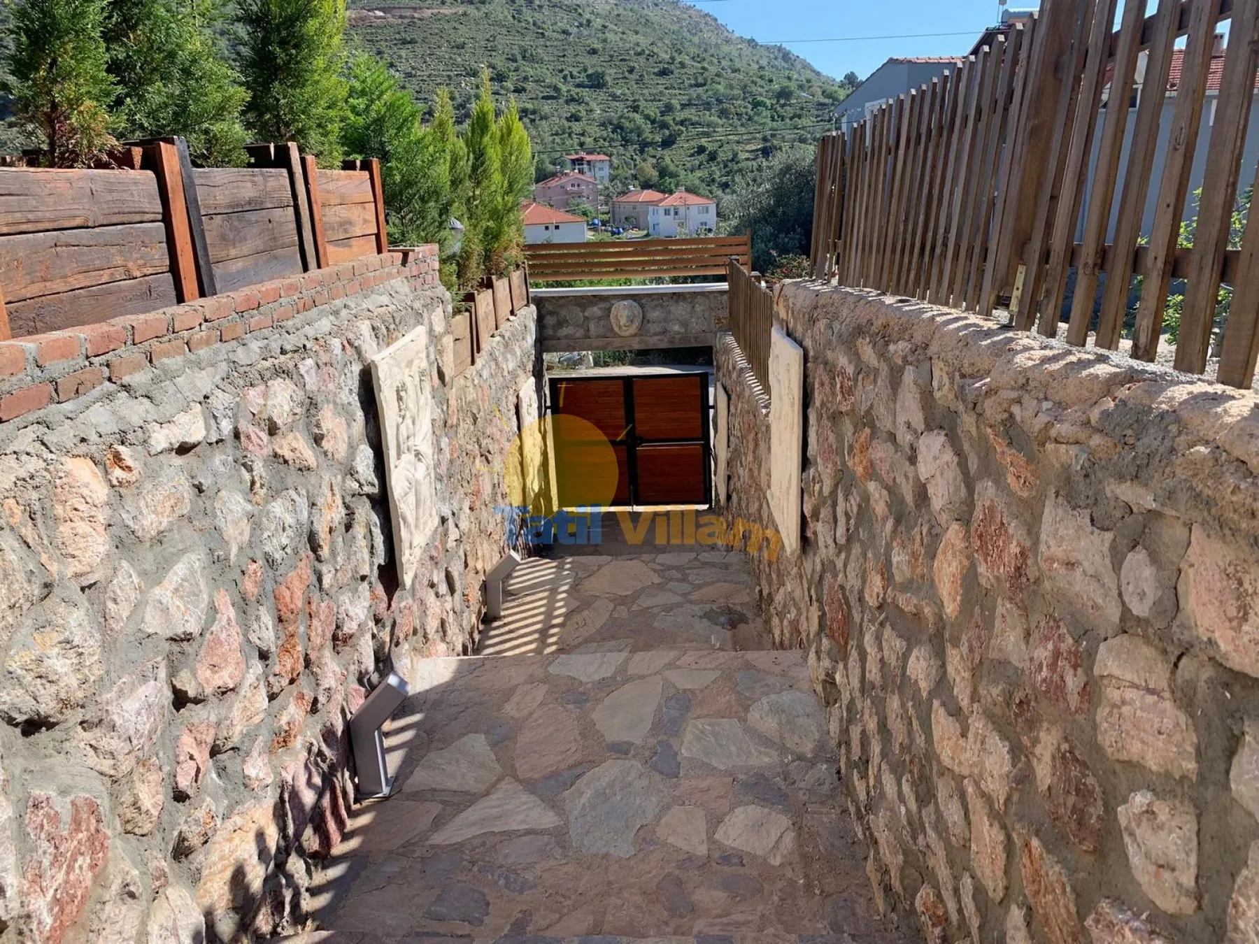 A stone walkway descends between walls toward a wooden door.