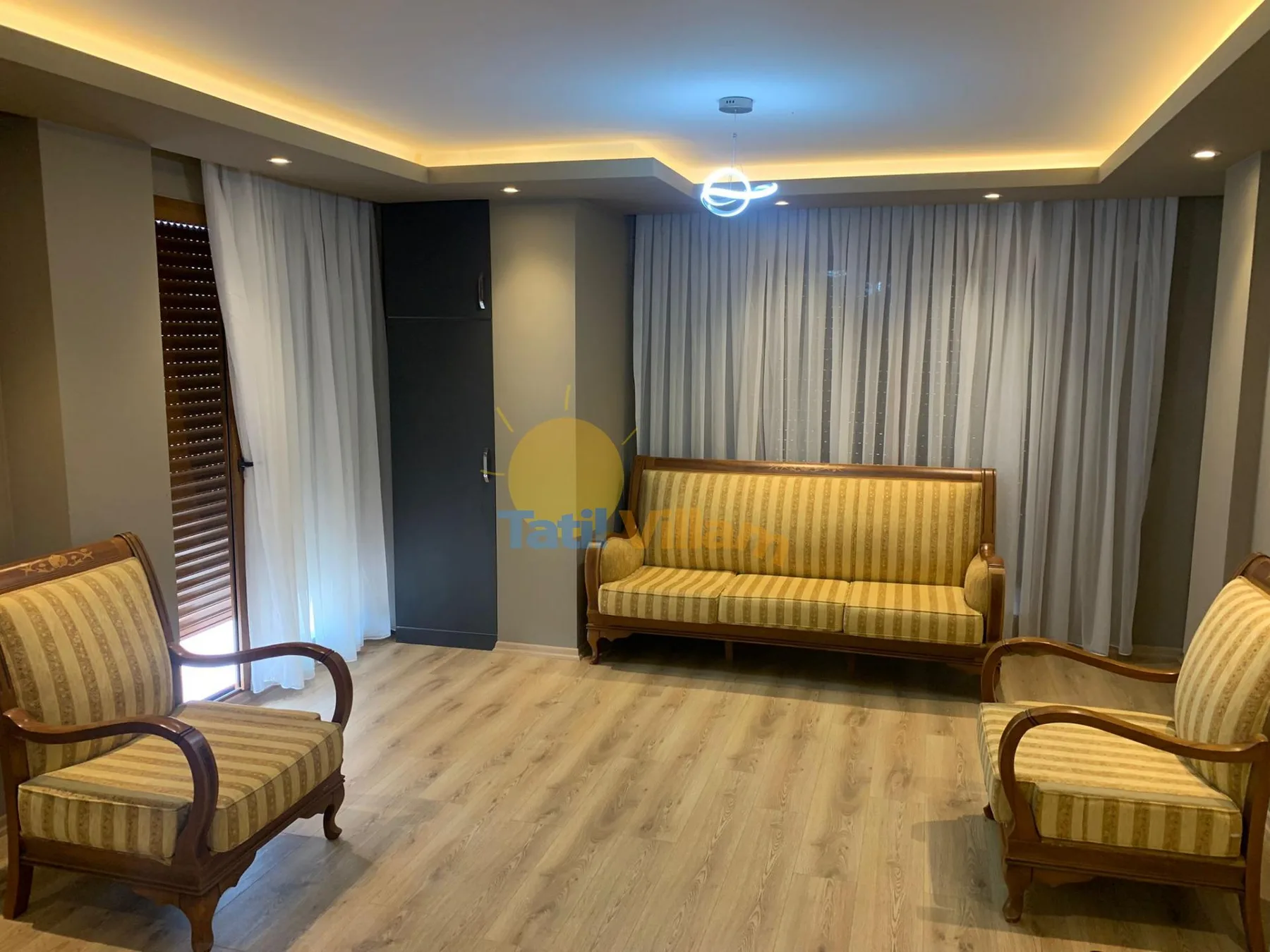 A furnished sitting room with striped seating and full-length curtains.