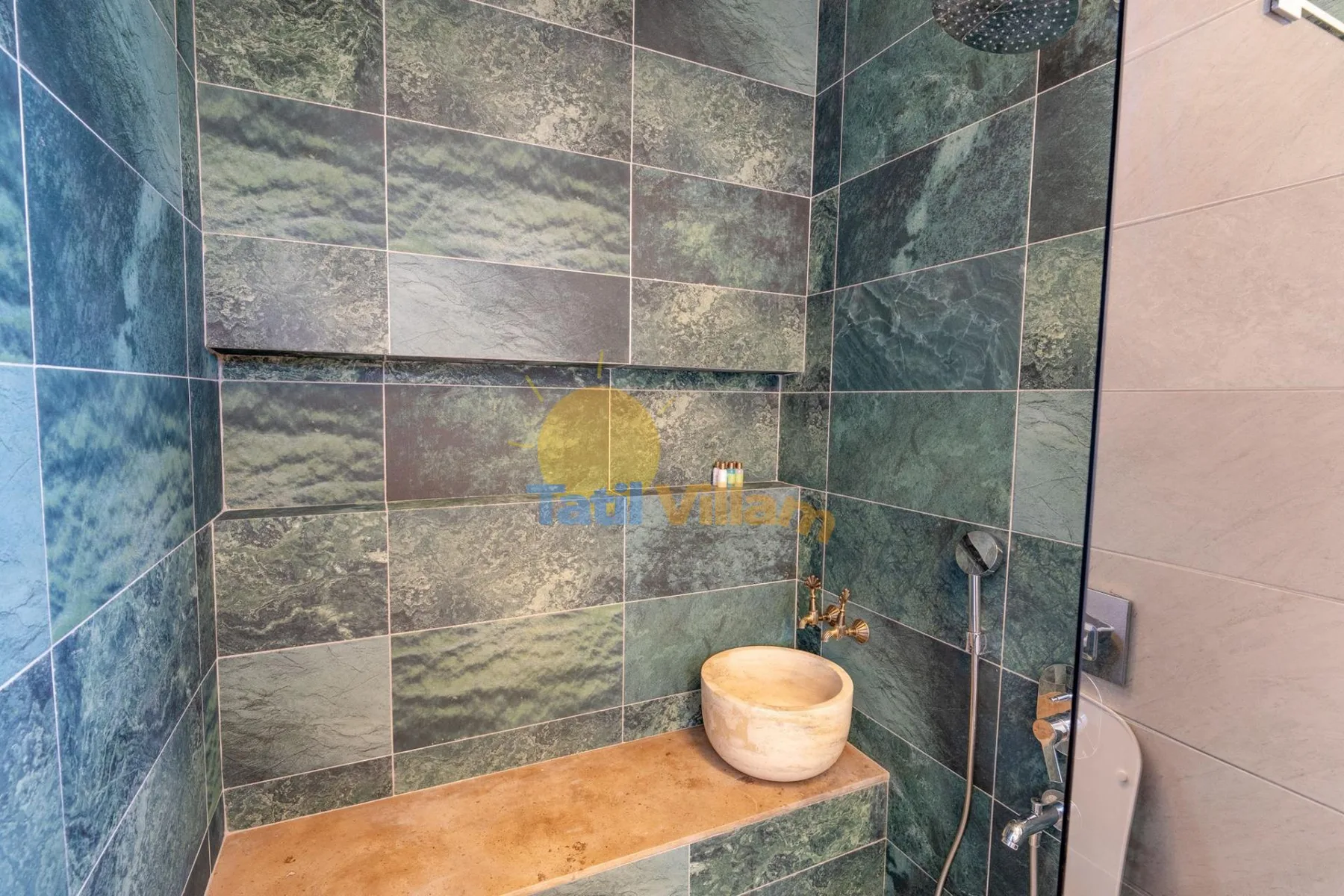 Una zona de ducha con azulejos, un cabezal de lluvia y un pequeño lavabo.