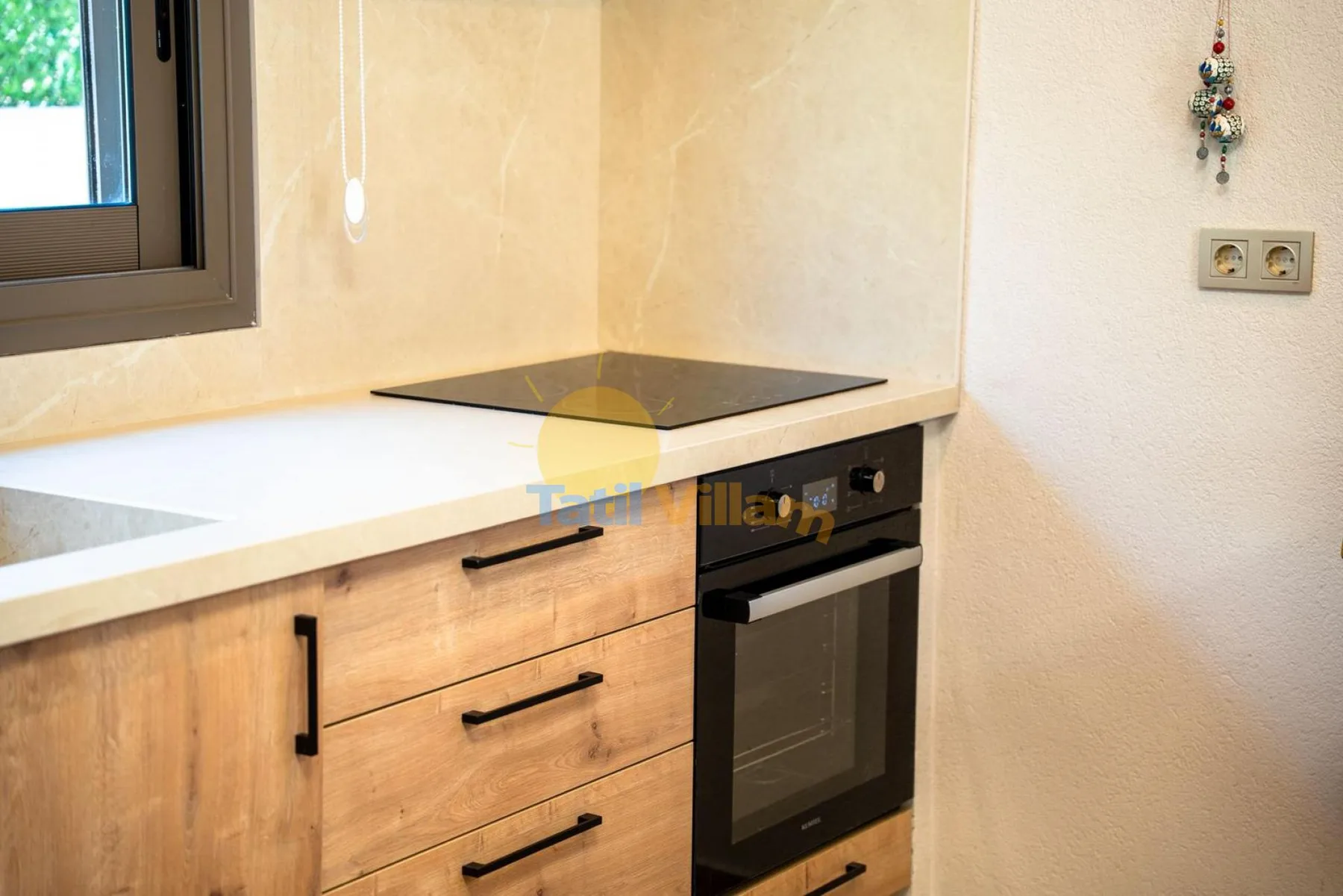 Una cocina compacta con placa de cocción, horno y armarios de madera clara.