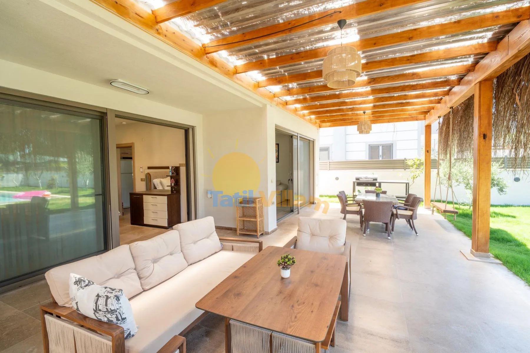Un patio cubierto tiene asientos al aire libre, una mesa de comedor y puertas corredizas de vidrio.