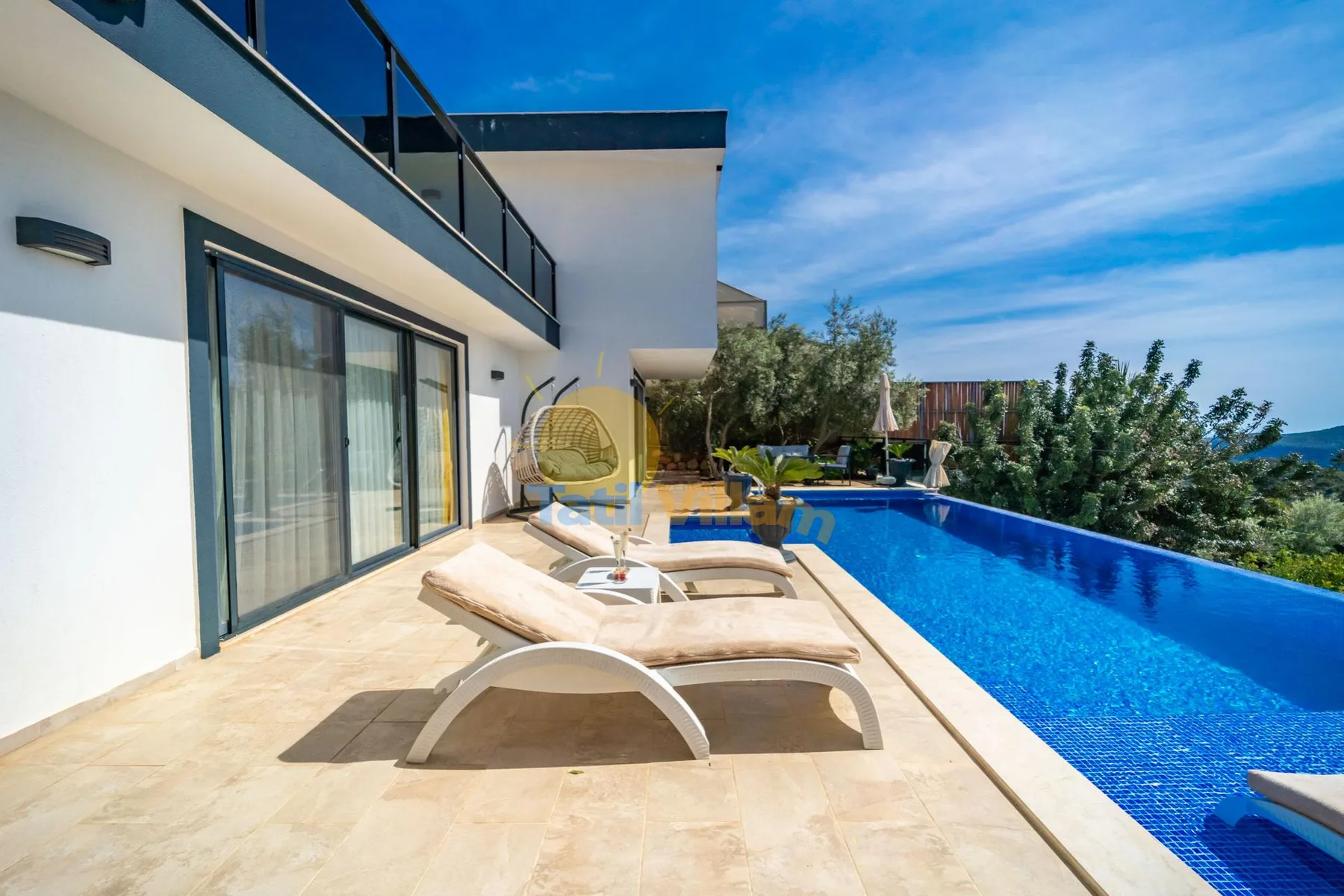 A sunny poolside patio with lounge seating beside a modern white building.