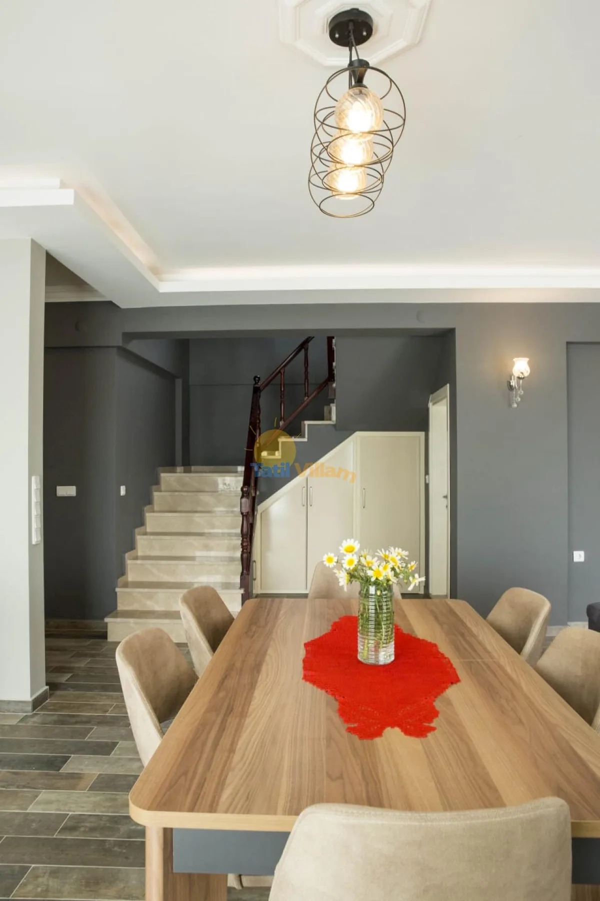 A dining area with a long wooden table and a staircase behind it.