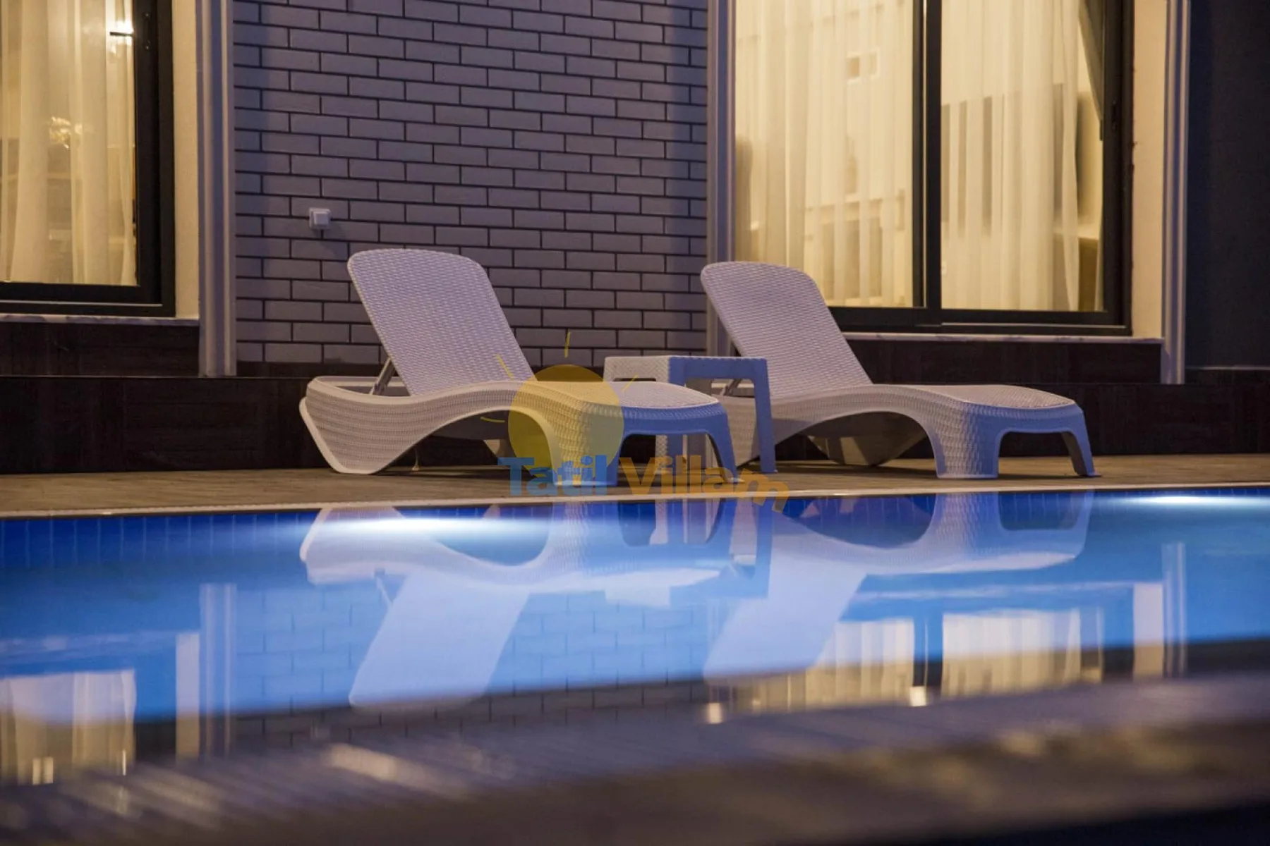 A swimming pool beside two lounge chairs and a small table.