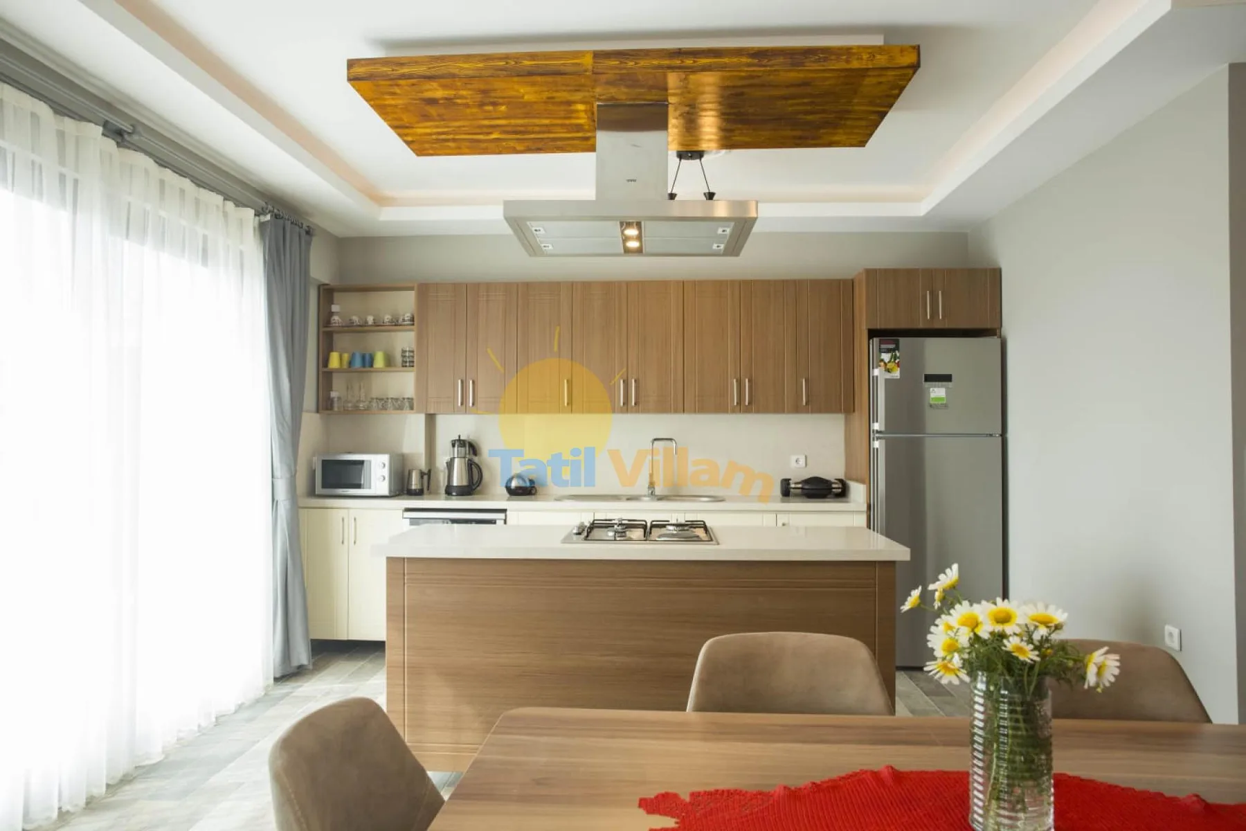 A bright kitchen with wood cabinetry, an island, and a dining table in the foreground.