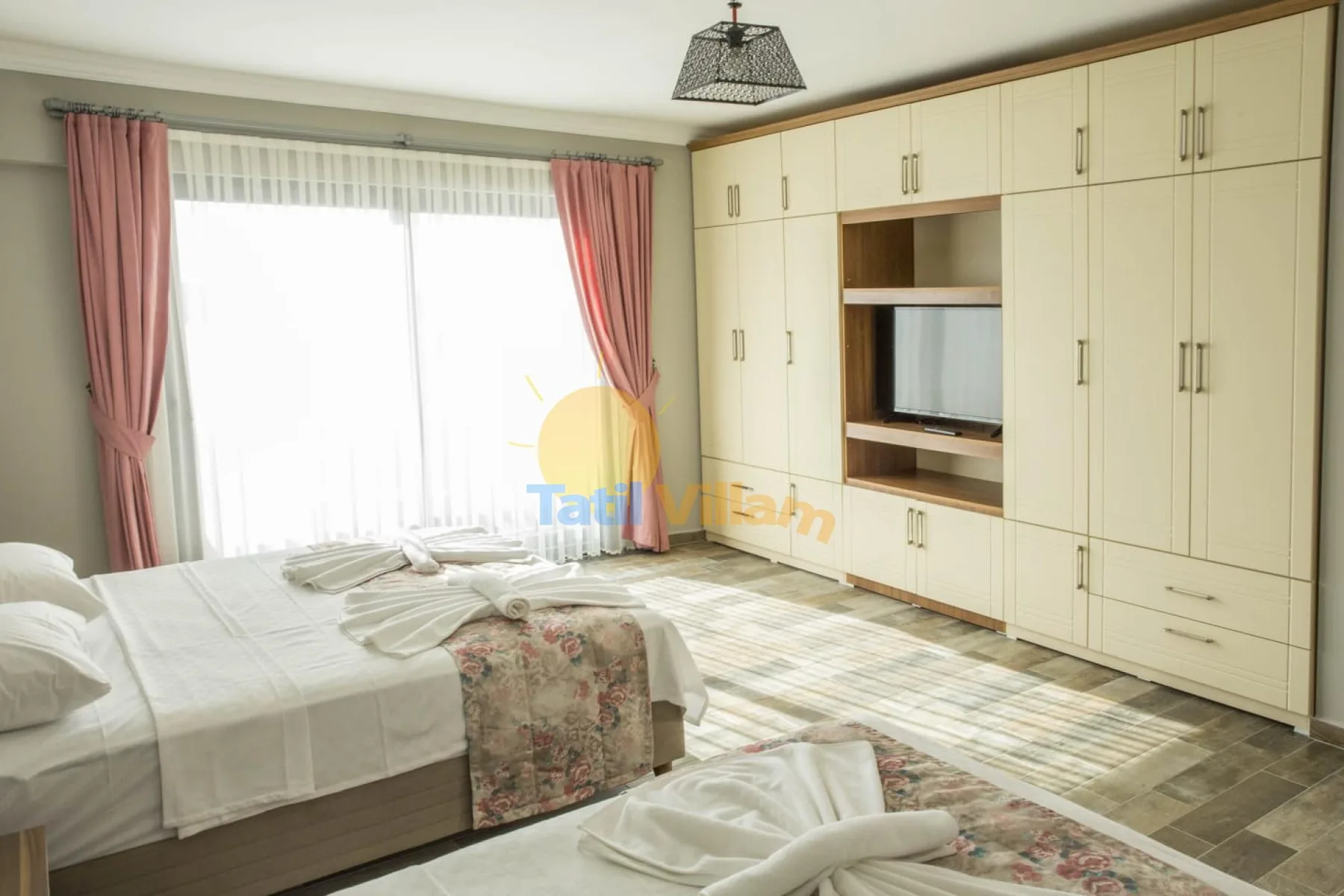 A bedroom with a bed beside a large curtained window and built-in cabinets.