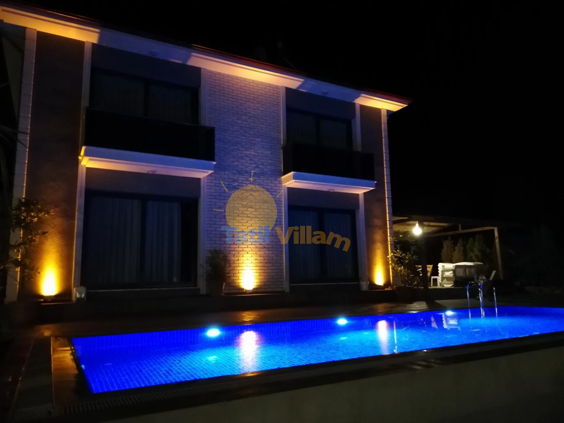 A modern building stands beside a brightly lit swimming pool at night.