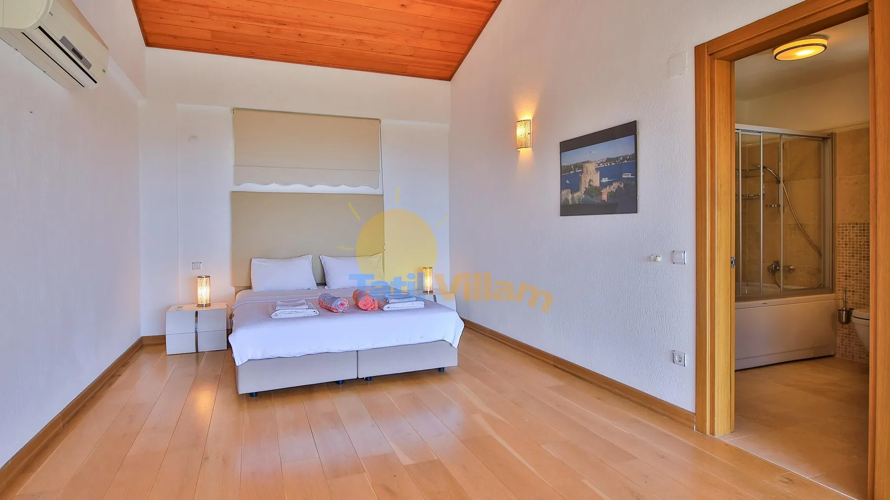 A bedroom with a bed, wooden flooring, and an adjoining bathroom.