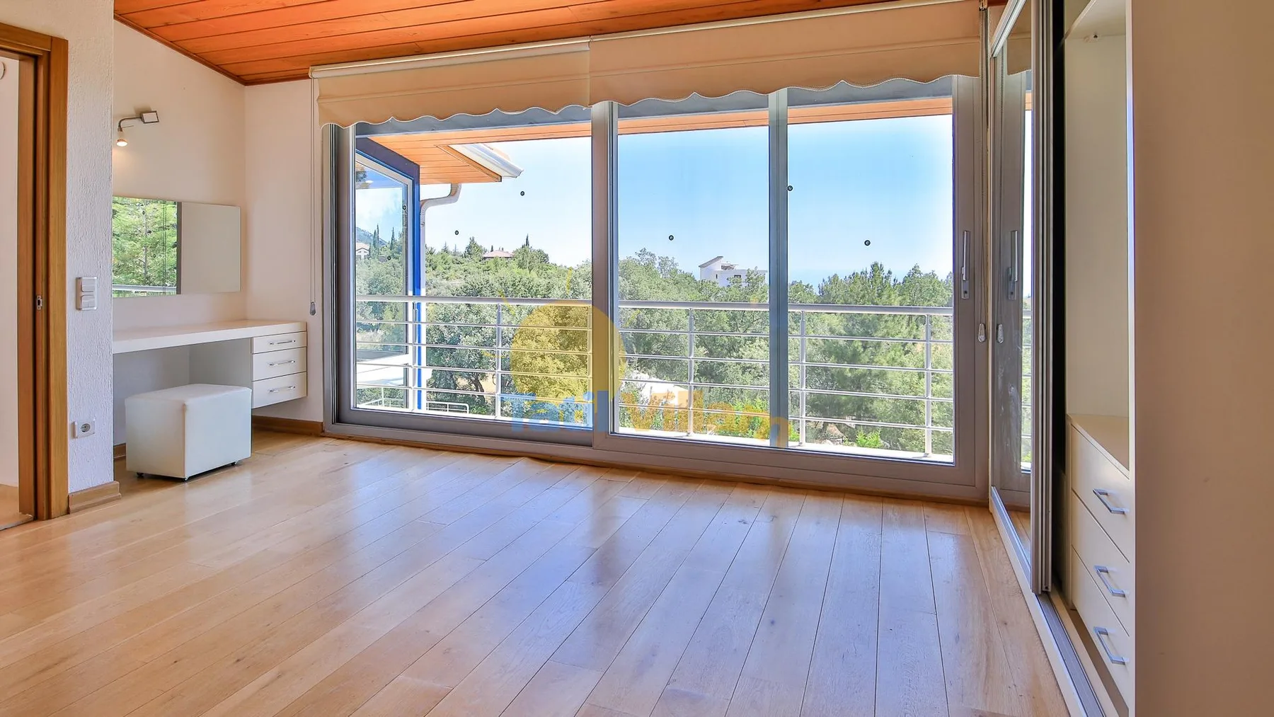 A bright empty room with wood flooring and large glass doors opening to a balcony.