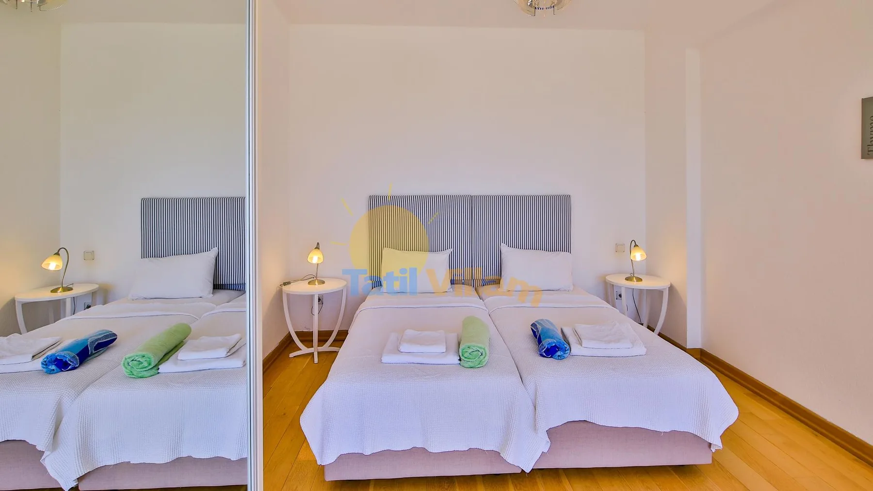A bright bedroom with two beds, bedside tables, and folded towels.
