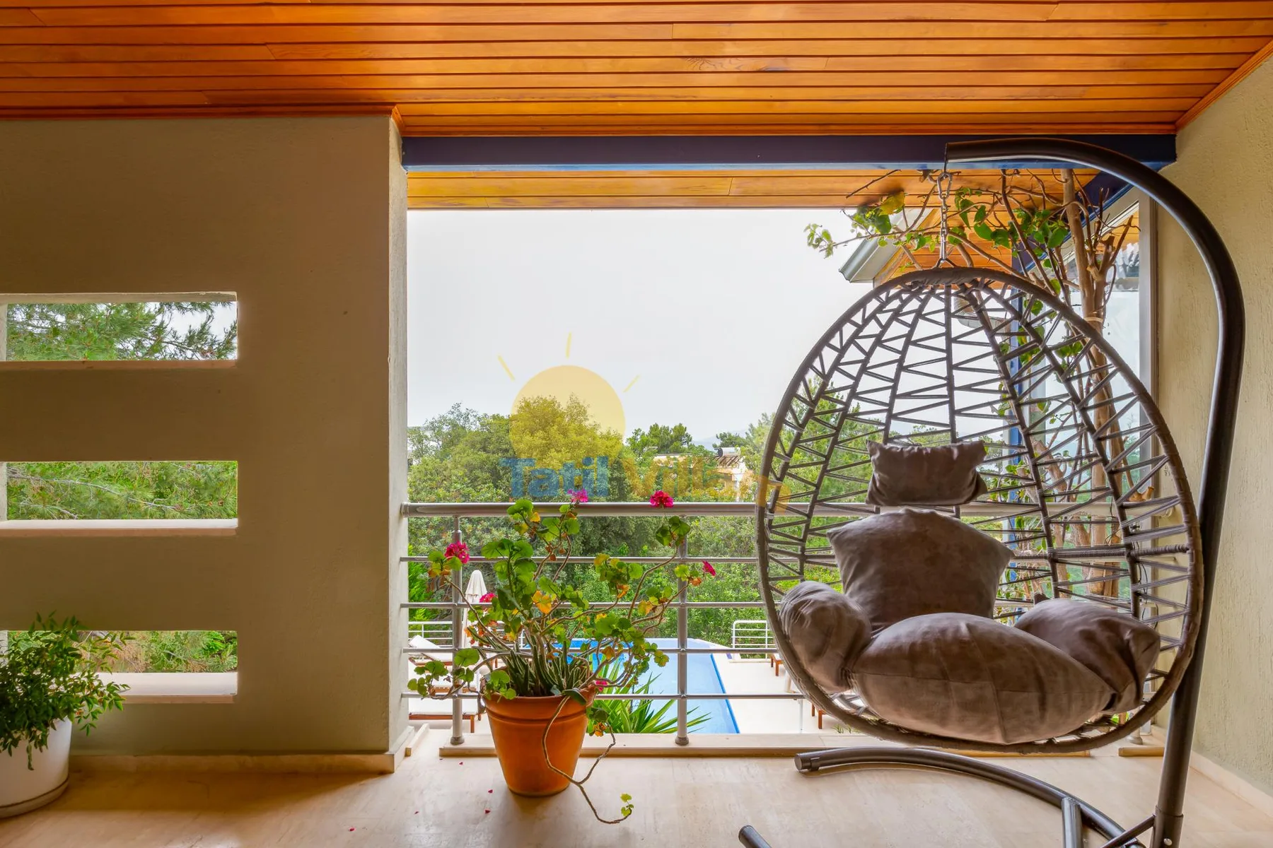 A covered balcony with a hanging lounge chair and potted plants overlooks greenery.
