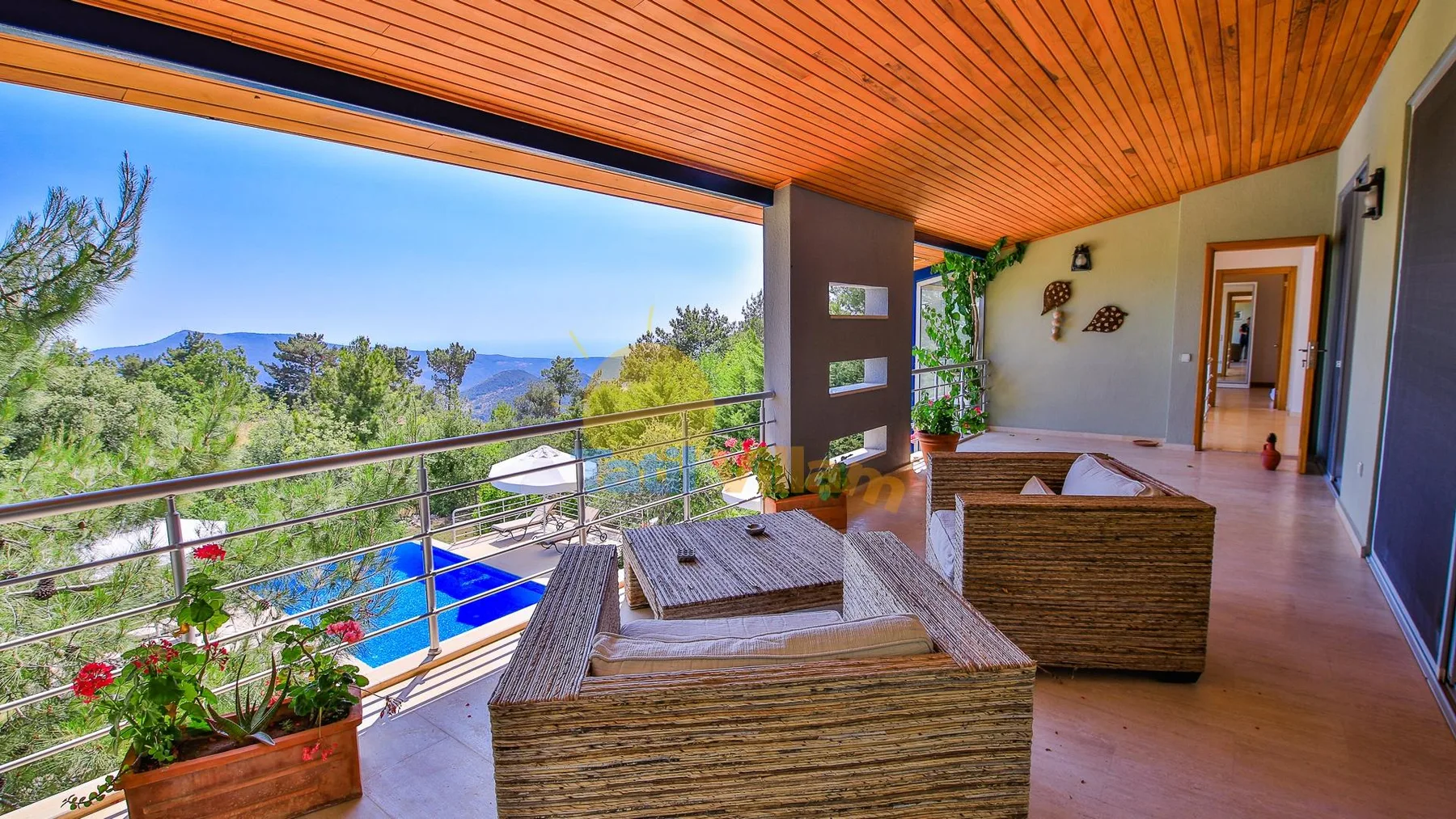 A covered balcony seating area overlooks a swimming pool and green hills.