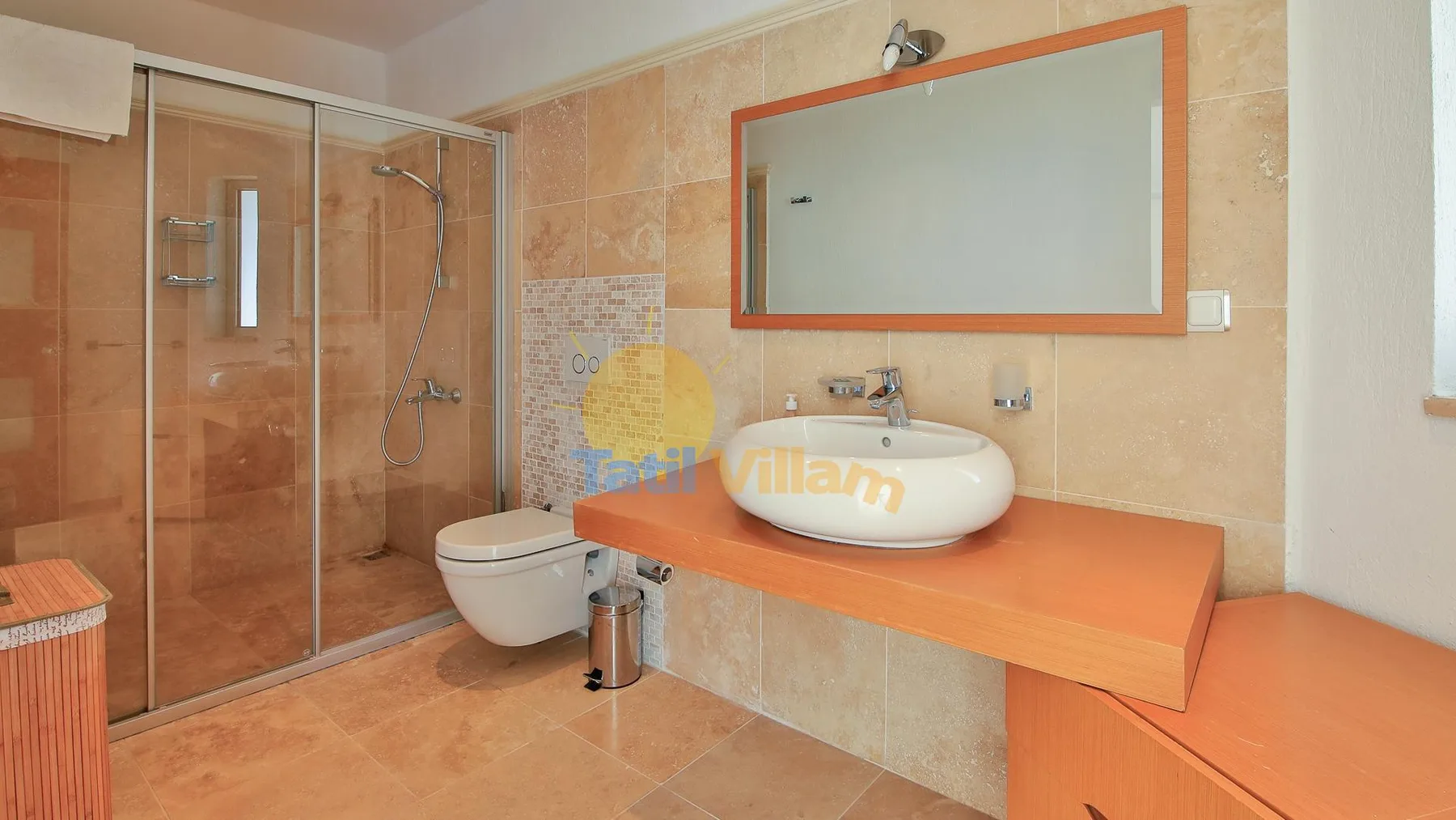 A tiled bathroom with a glass shower, toilet, and basin on an orange counter.